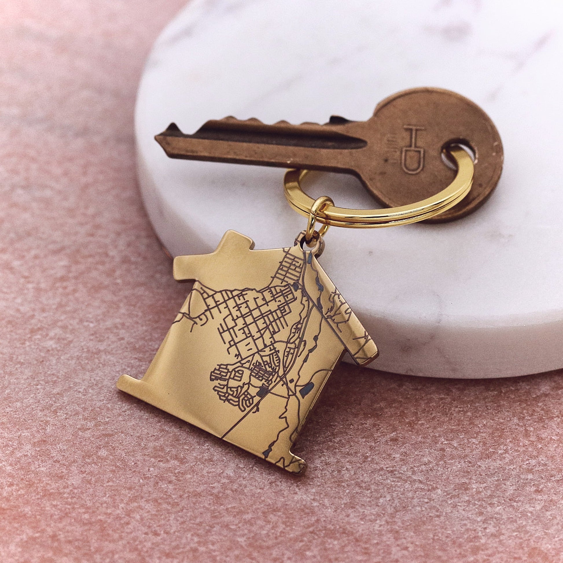 Gold keychain with map design attached to a key on a pink surface.