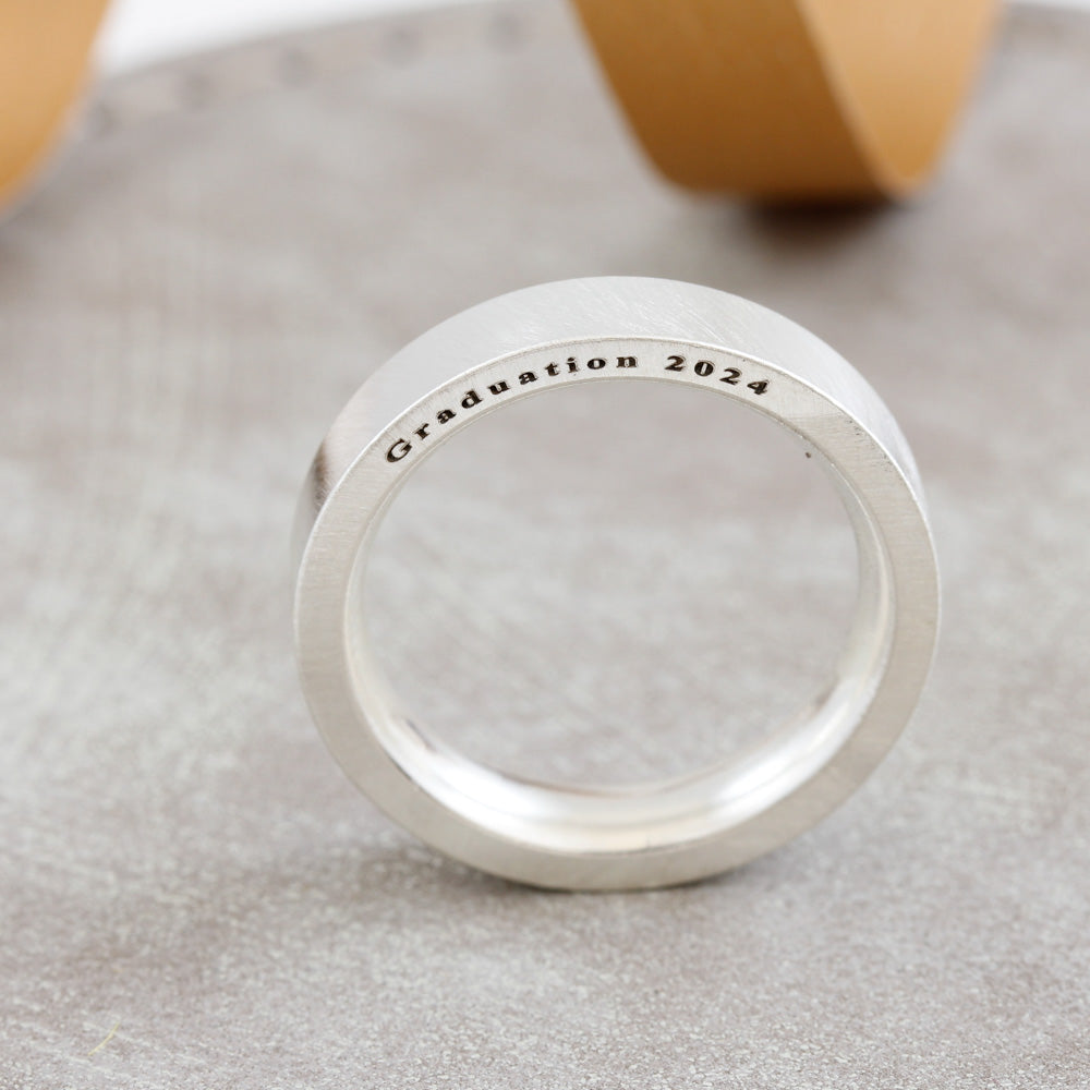 Silver ring with 'Graduation 2024' engraving on a textured surface