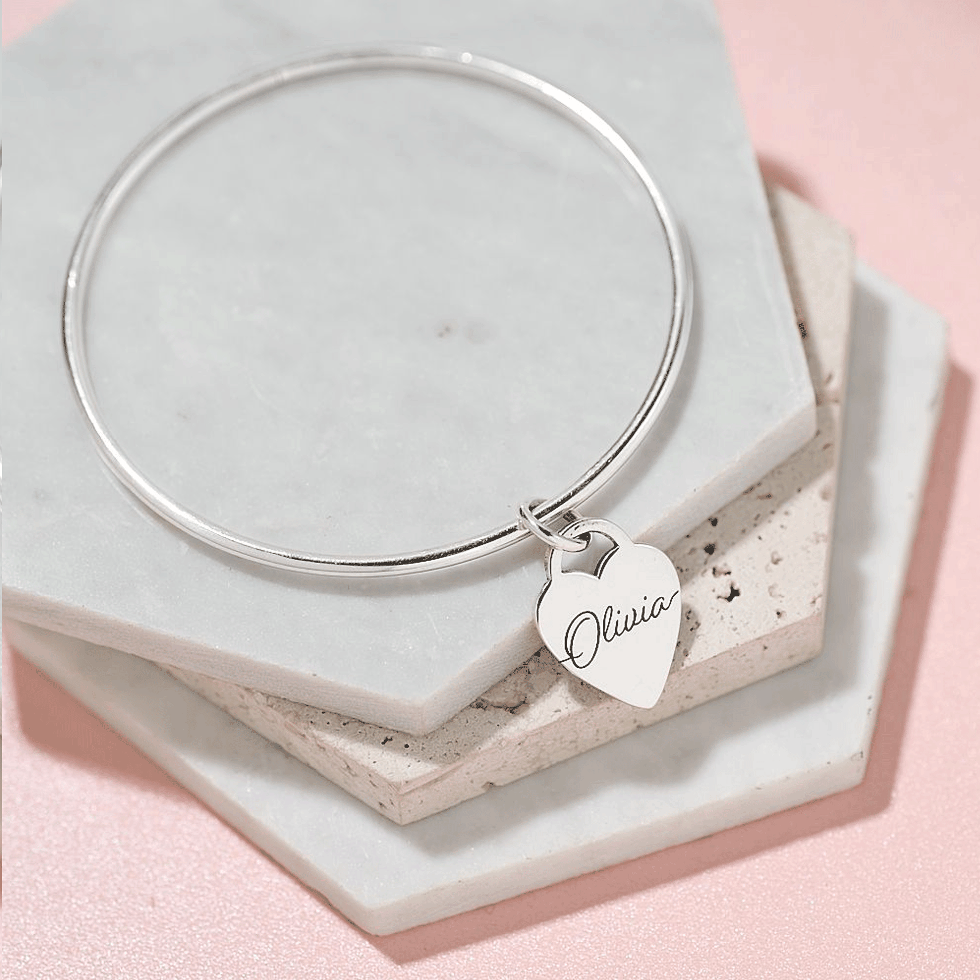 Silver bangle with a heart-shaped charm engraved with name on a marble surface