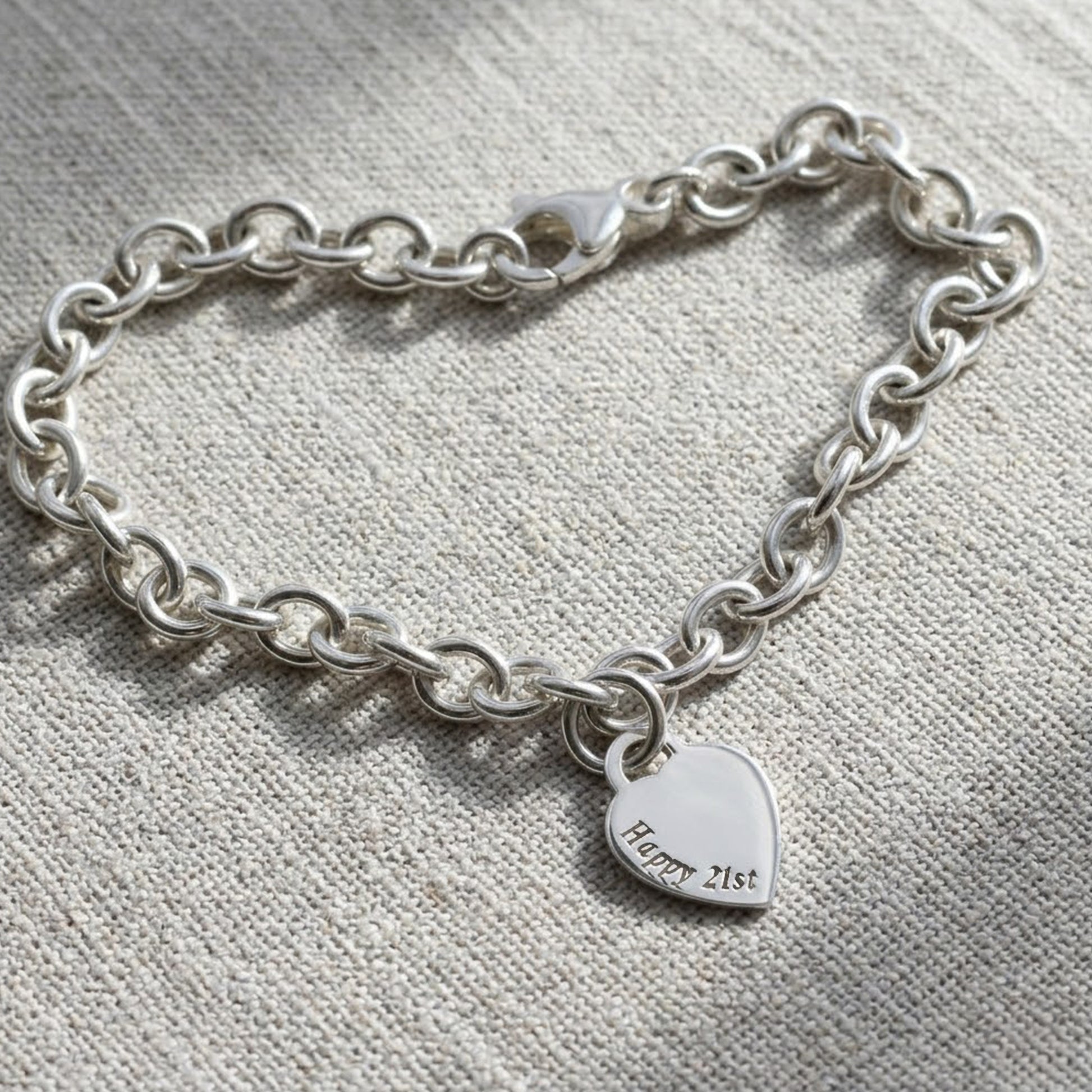silver charm bracelet with engraved heart charm on a fabric background