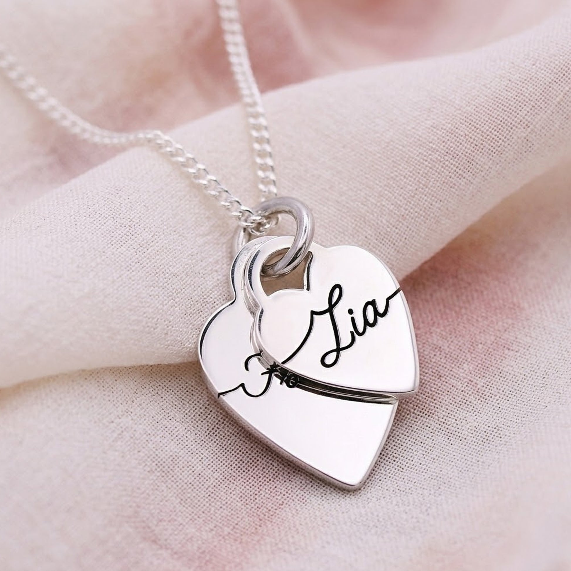 Silver heart-shaped pendant with 'Lia' engraved on a soft pink fabric background