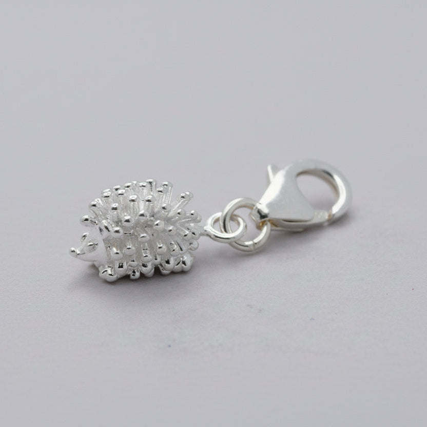 Silver charm resembling a hedgehog on a green and beige background
