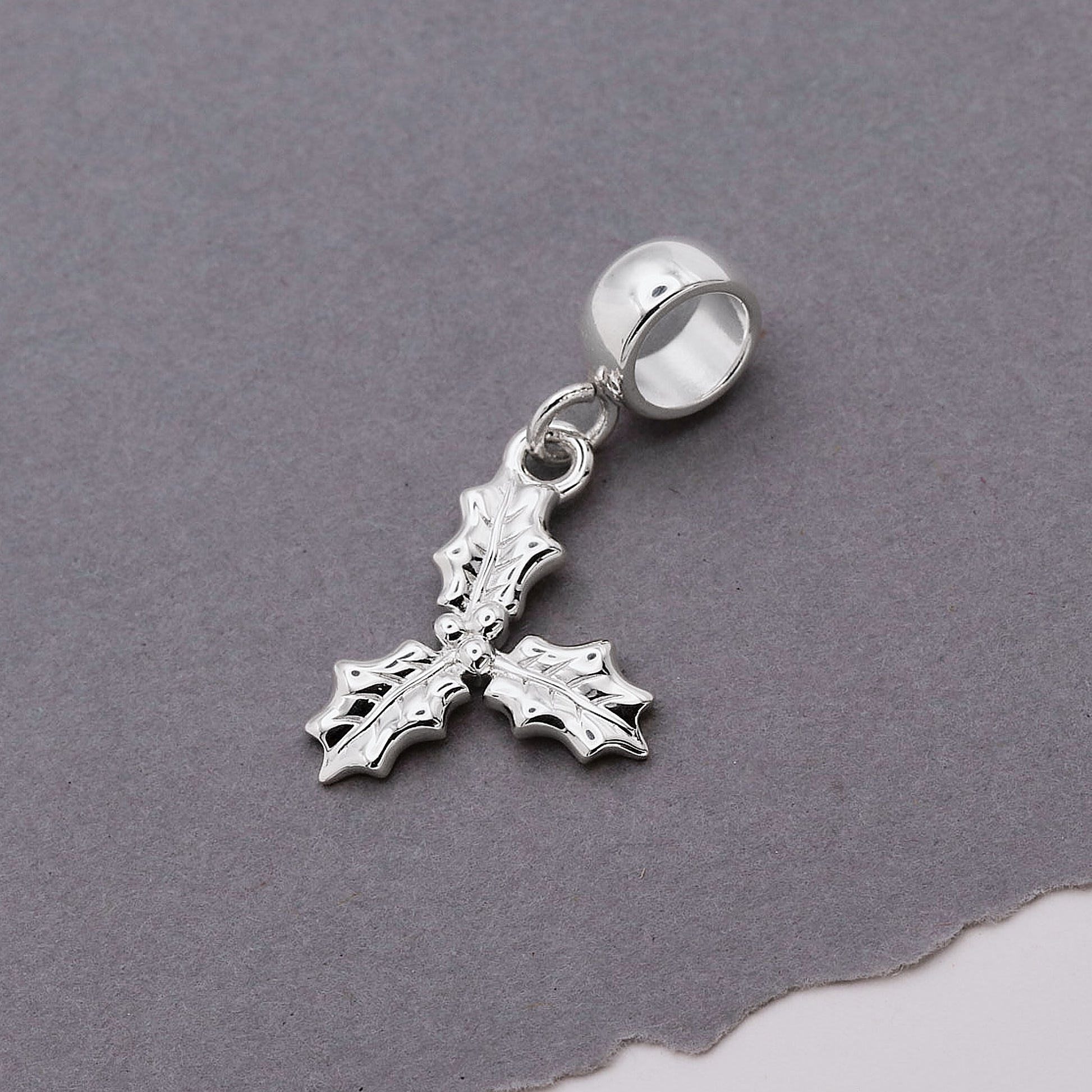 Silver holly leaf charm on a gray background