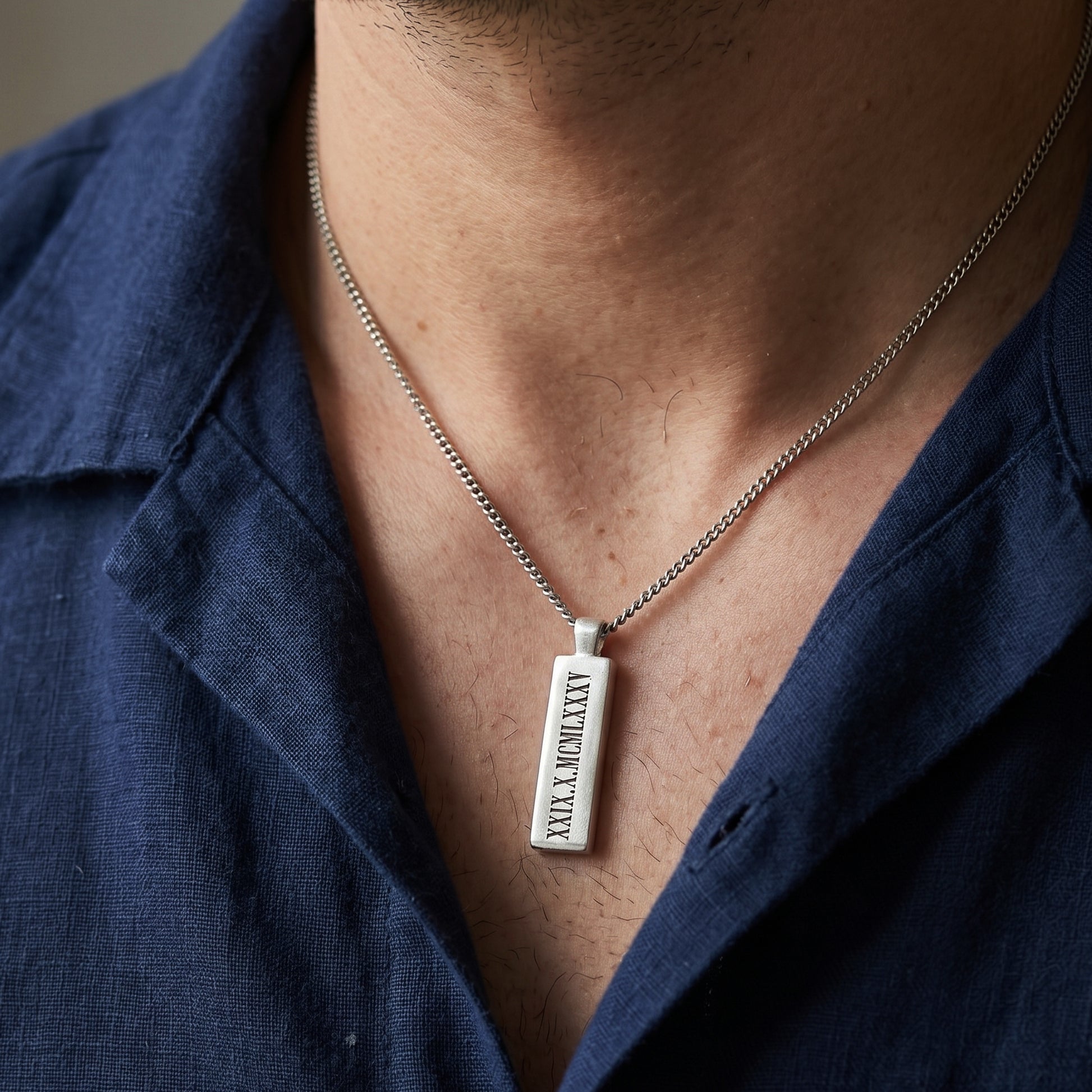 Person wearing a necklace with a pendant on a plain background