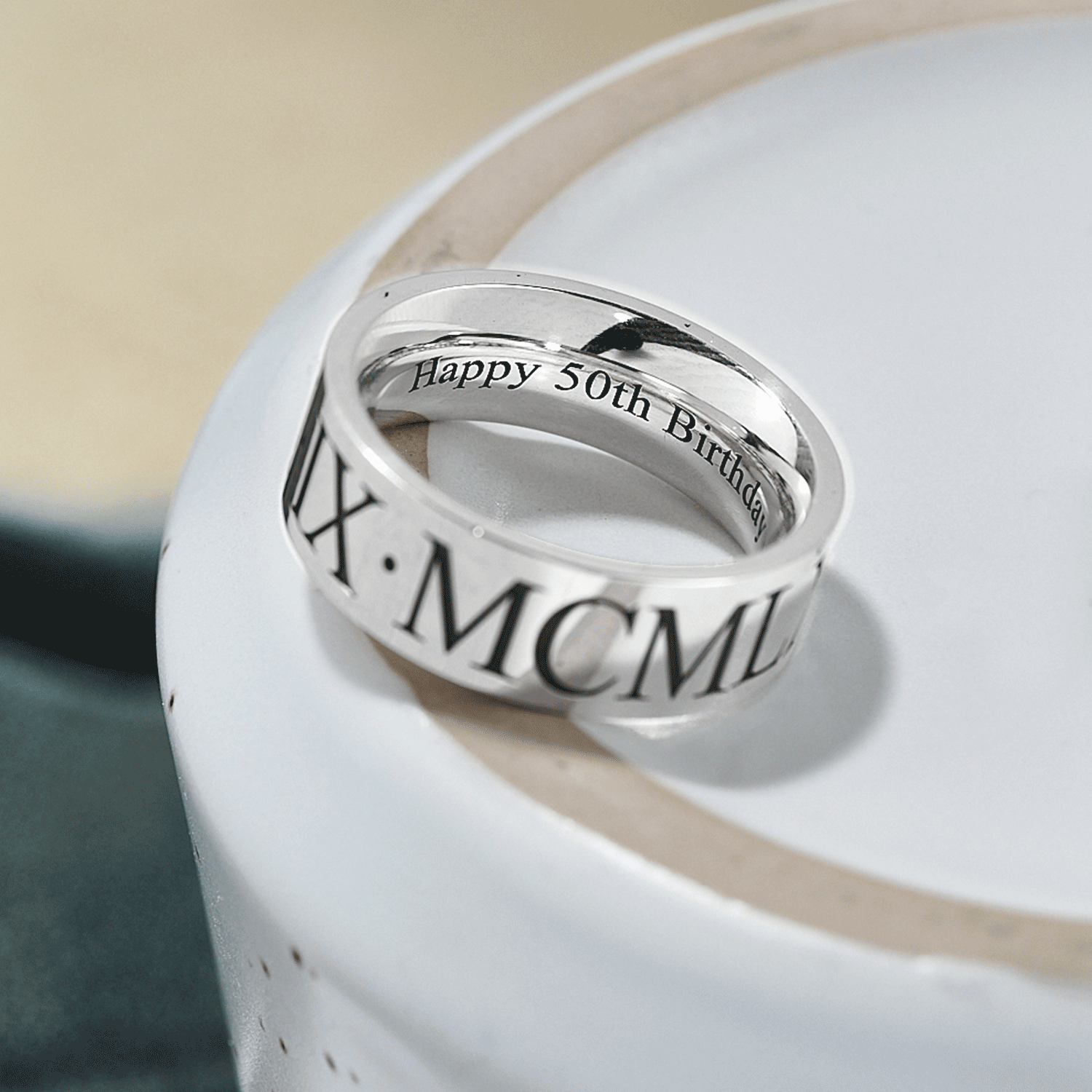 Silver ring with Roman numeral and 'Happy 50th Birthday' engraving on a white surface.
