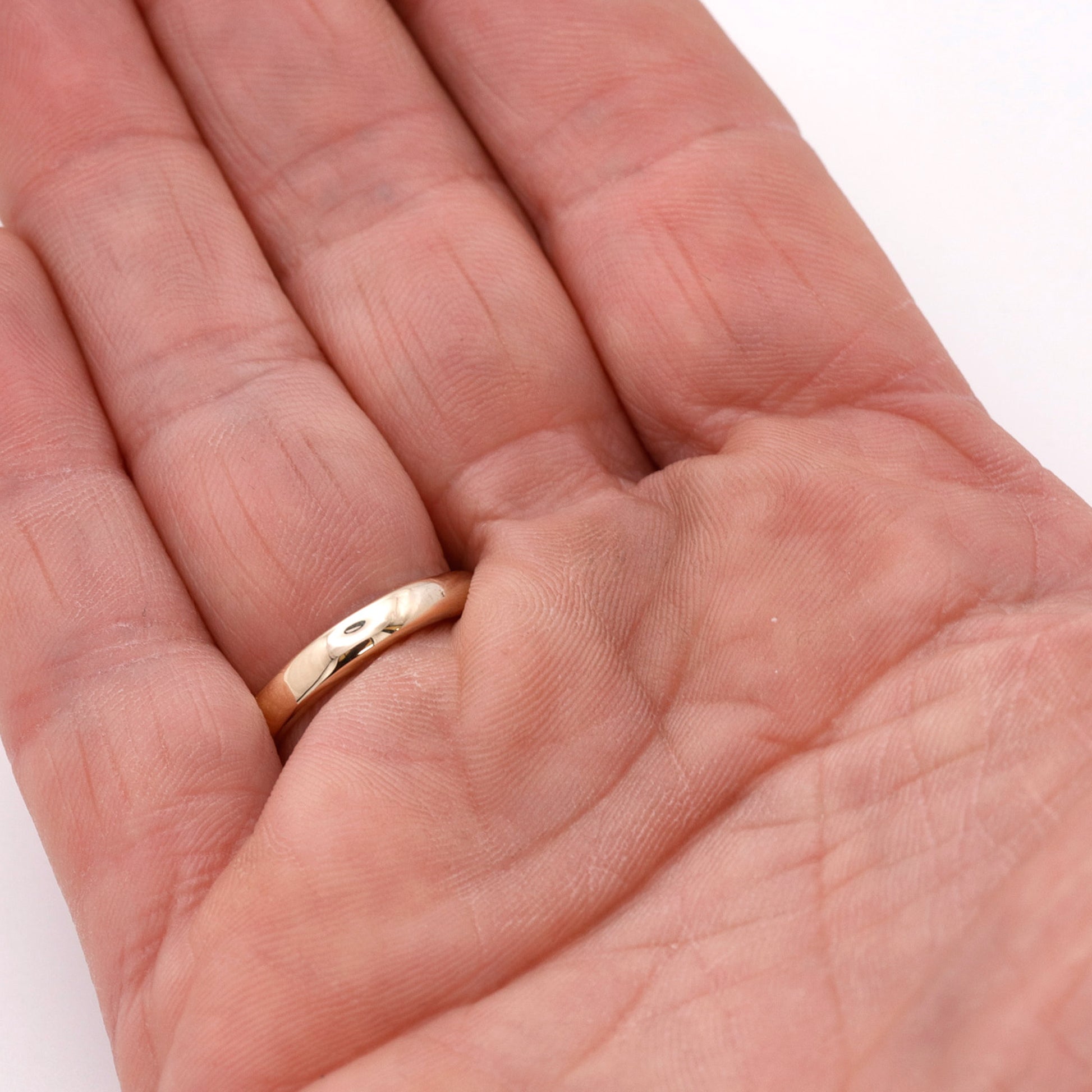 Gold ring on a person's finger with a plain background