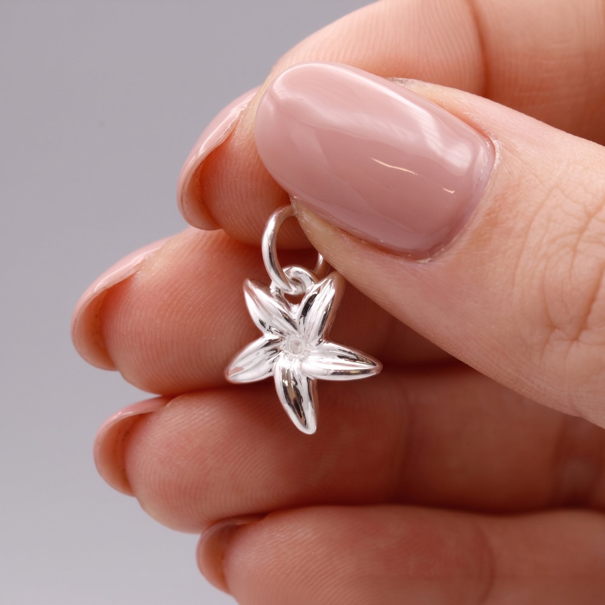 Silver flower-shaped pendant held between fingers against a neutral background