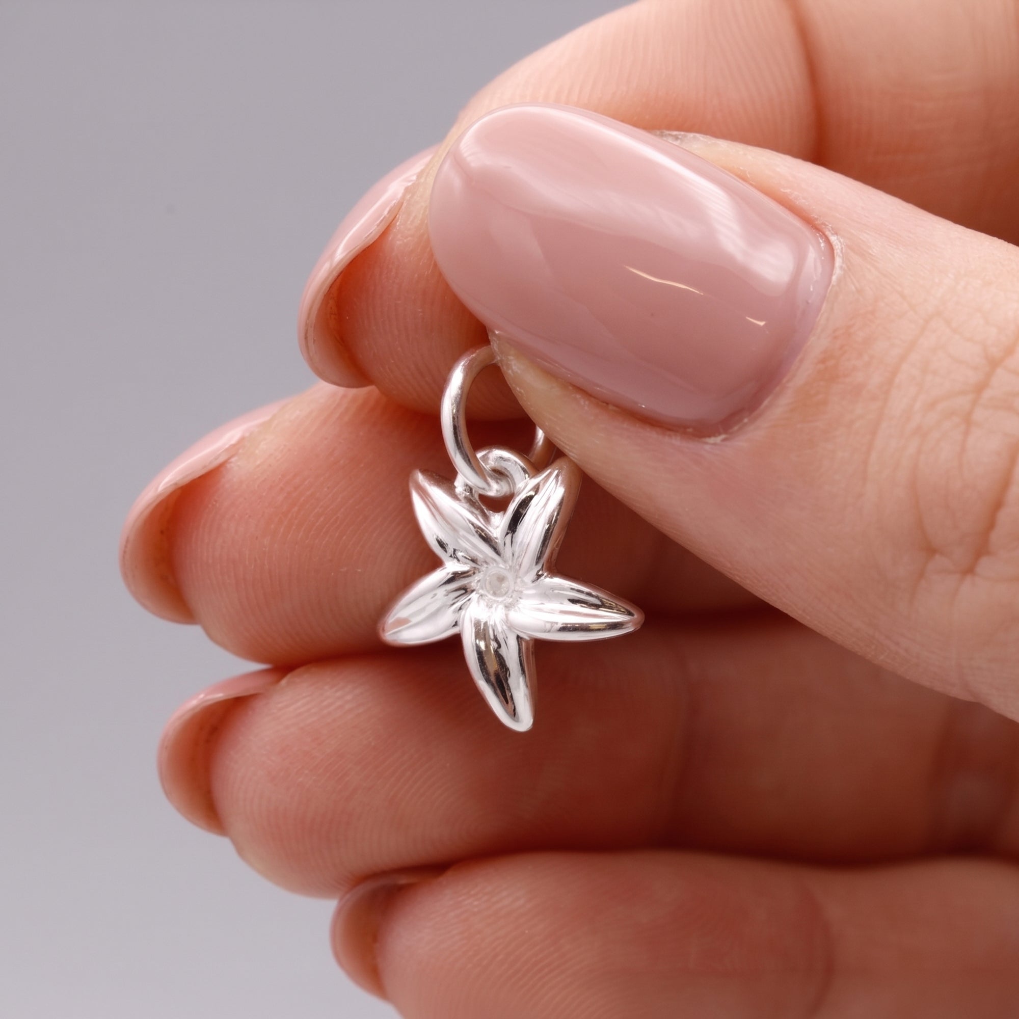 Silver flower-shaped pendant held between fingers against a neutral background