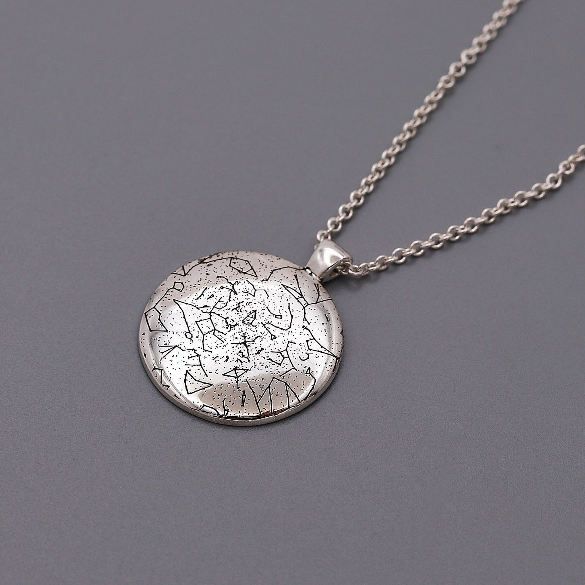 Silver star map necklace with a textured round pendant on a gray background