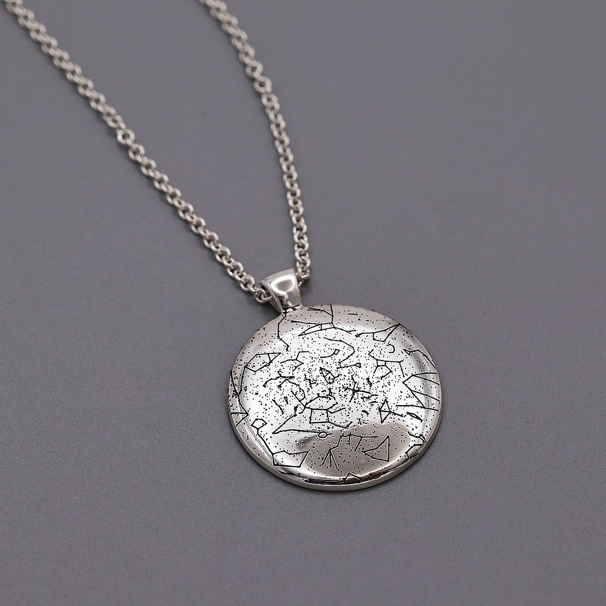 Silver star map necklace with a textured round pendant on a gray background