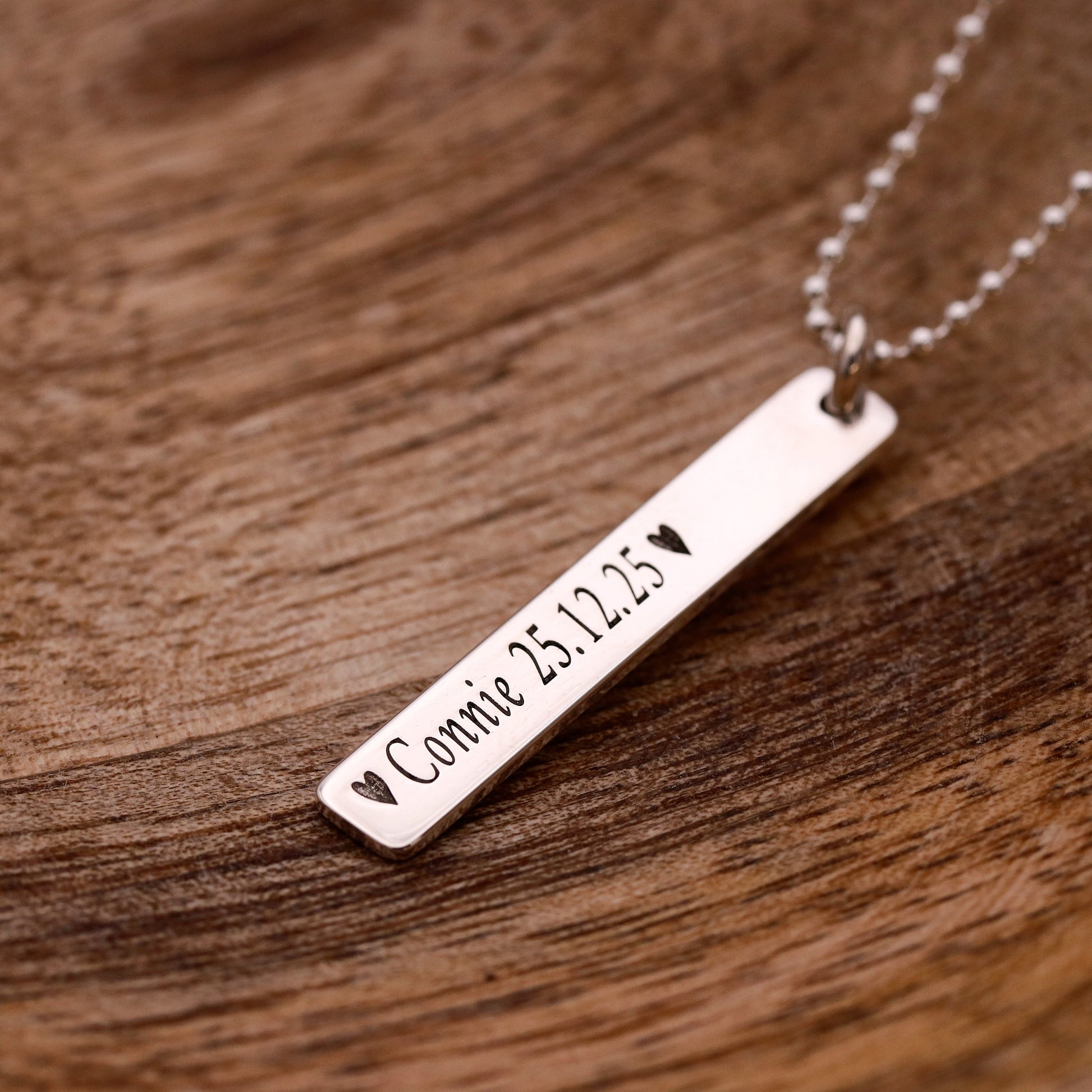 Silver bar necklace with engraved text on a wooden surface