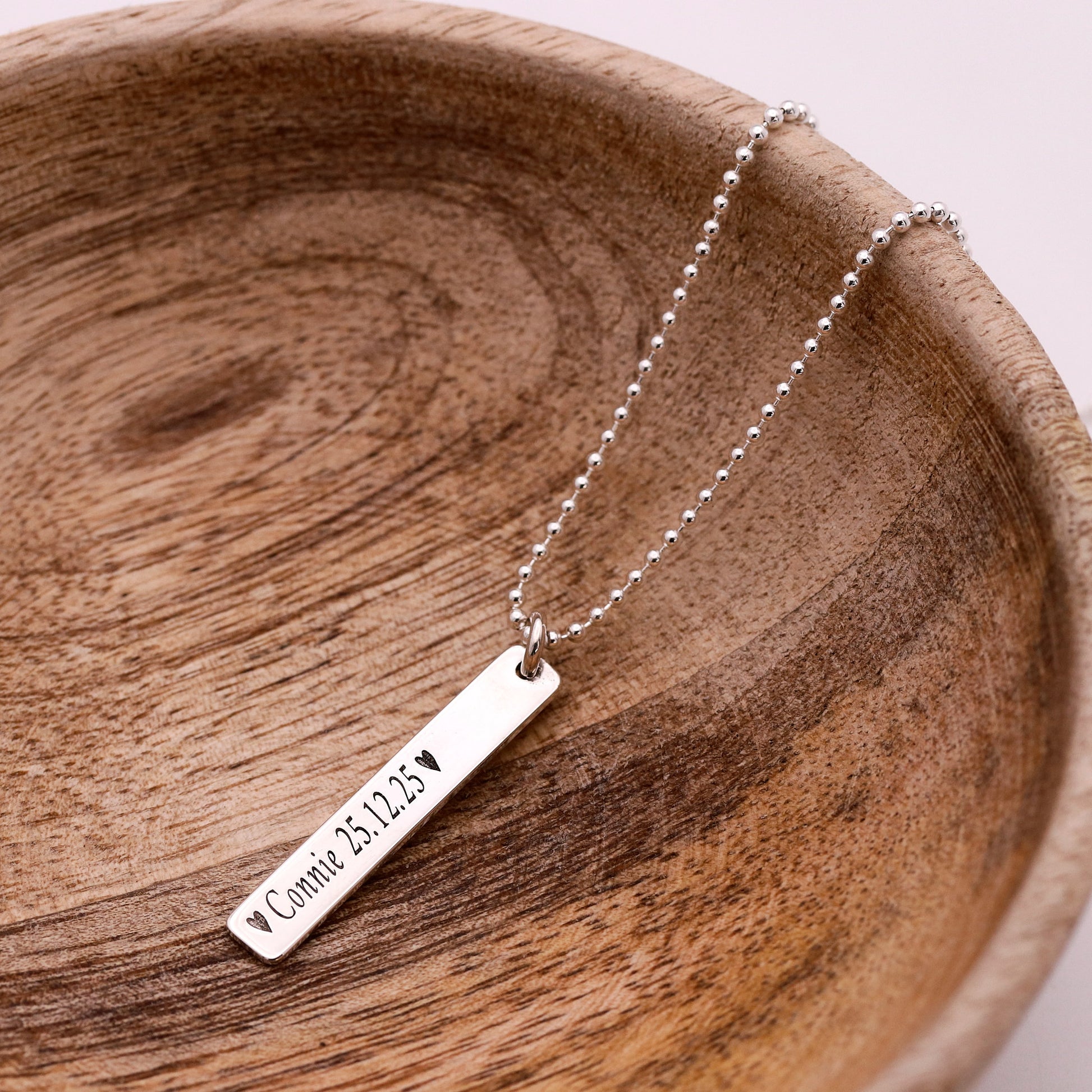 Silver necklace with a bar pendant on a wooden surface
