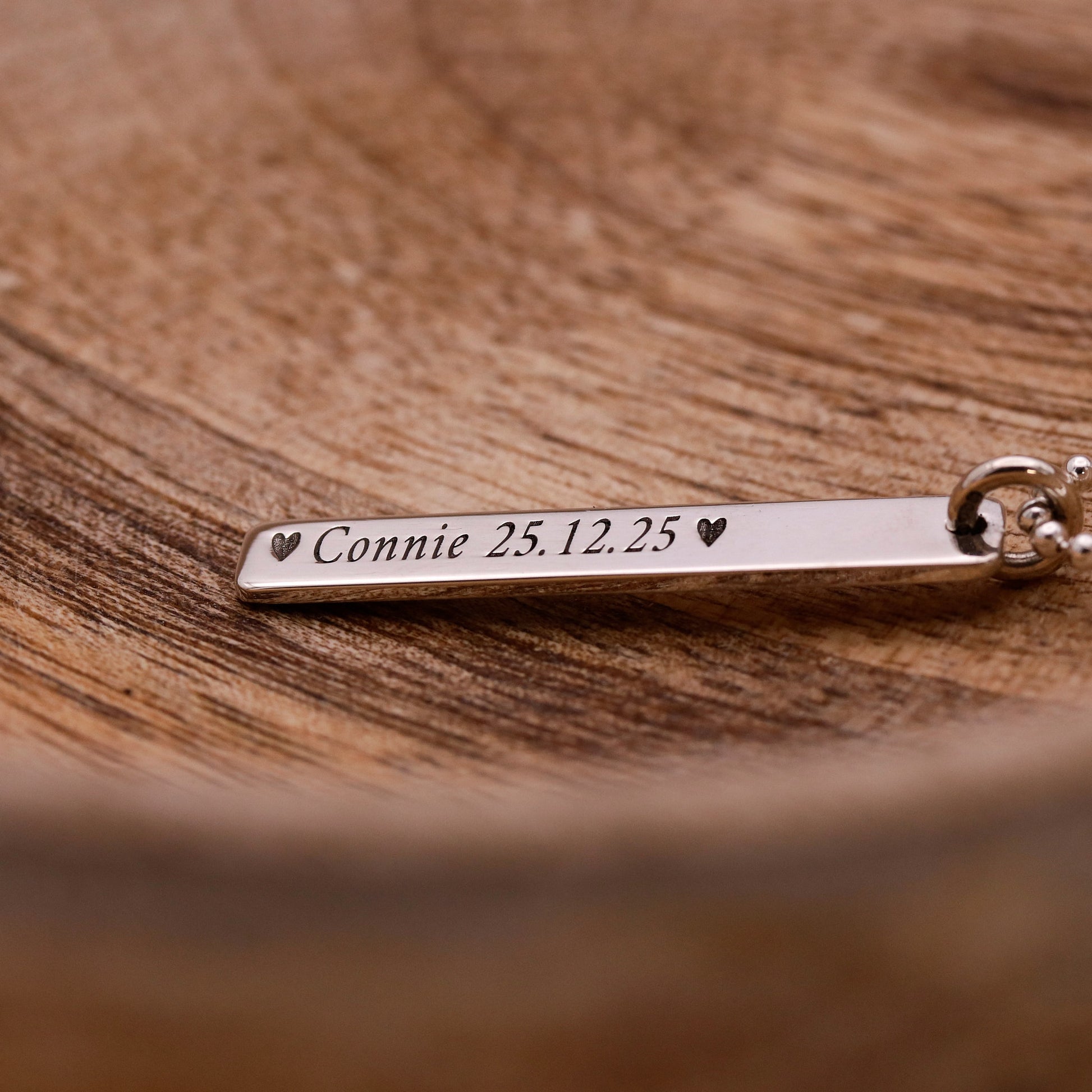Silver bar necklace with engraved text on a wooden surface