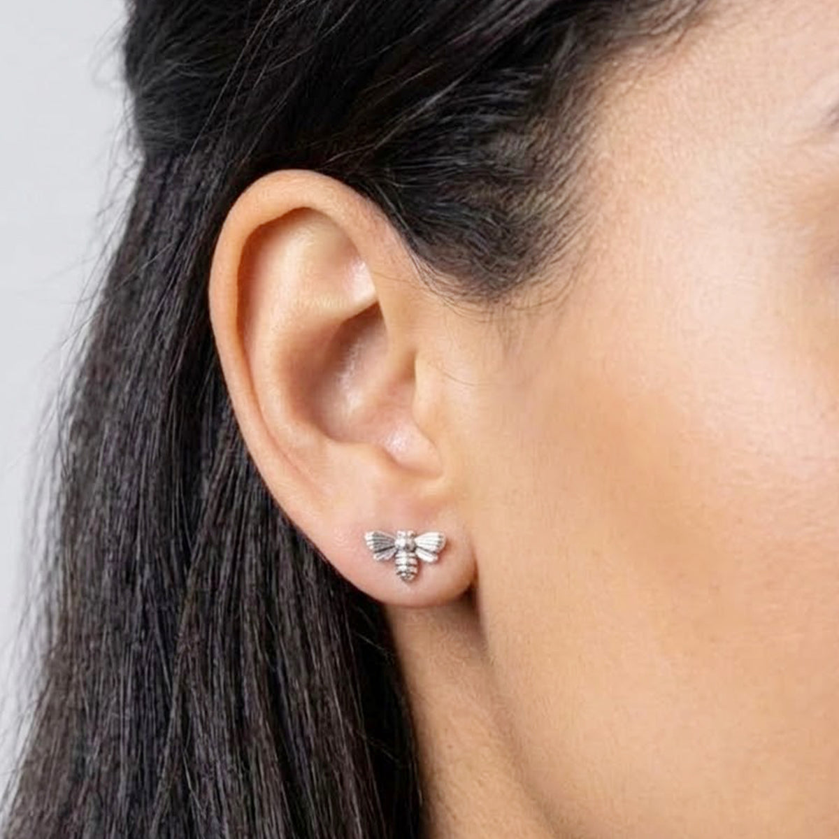 A close-up of a model's ear wearing a small silver bee stud earring.