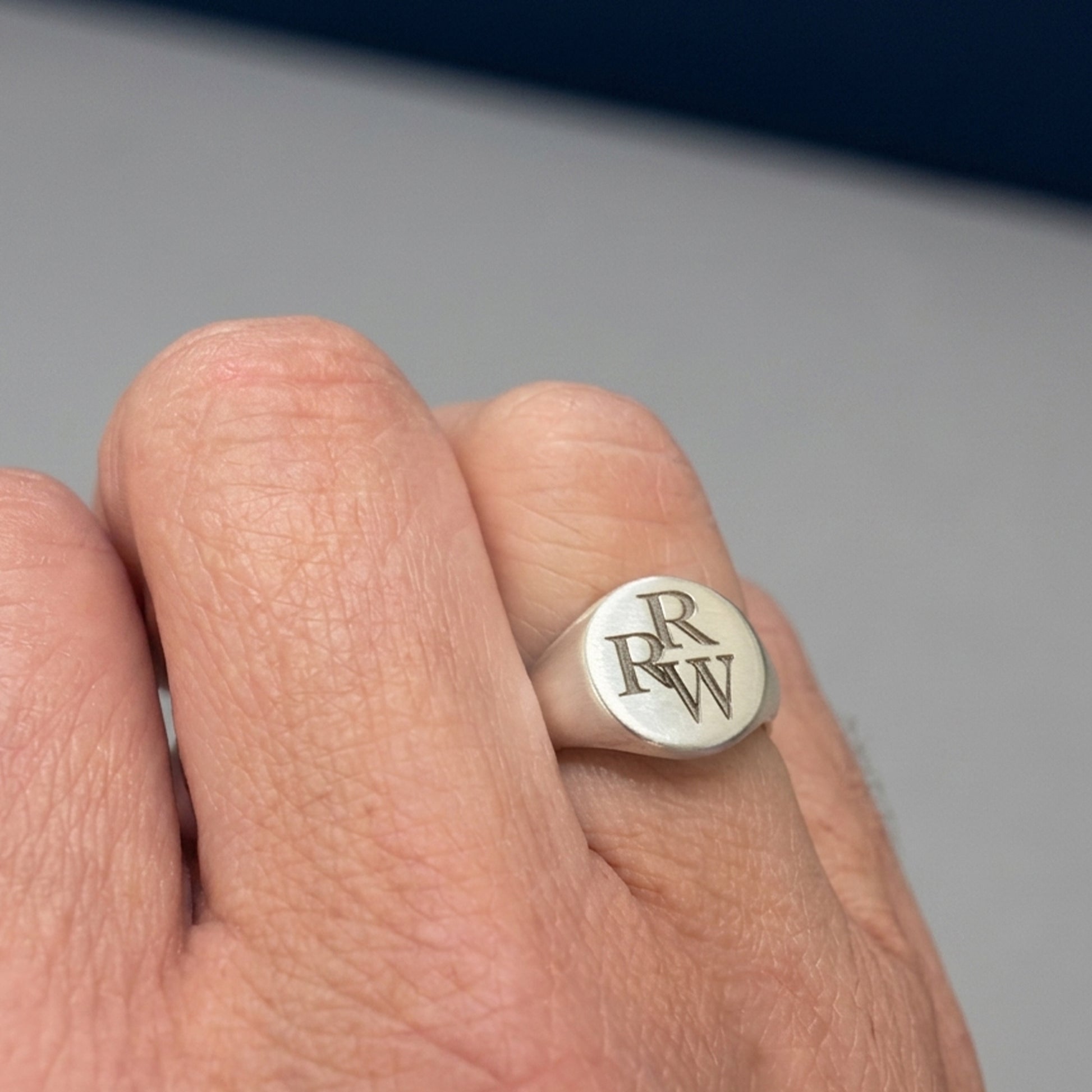Silver ring with 'RW' initials on a person's finger against a neutral background