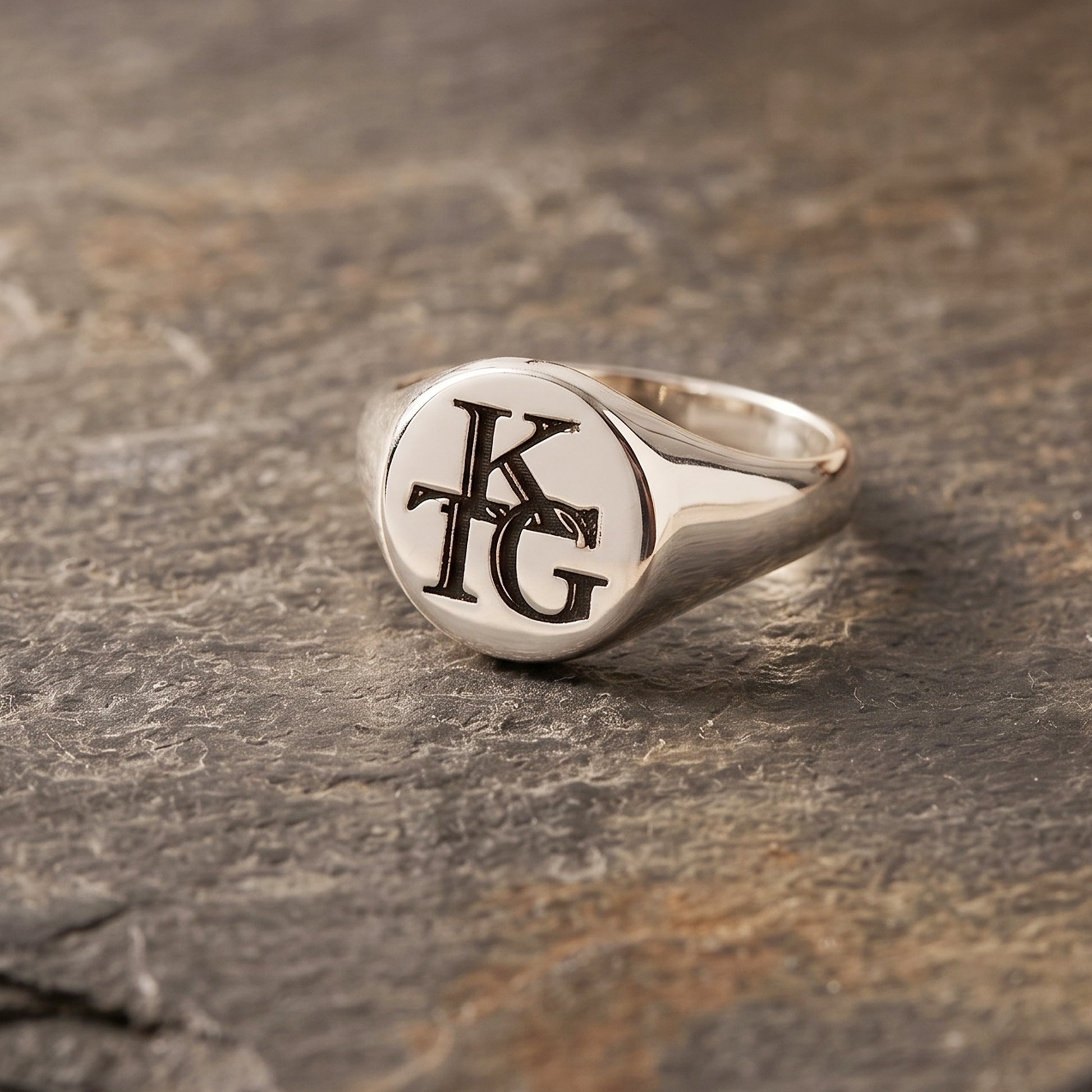 Silver ring with 'KG' initials on a stone surface