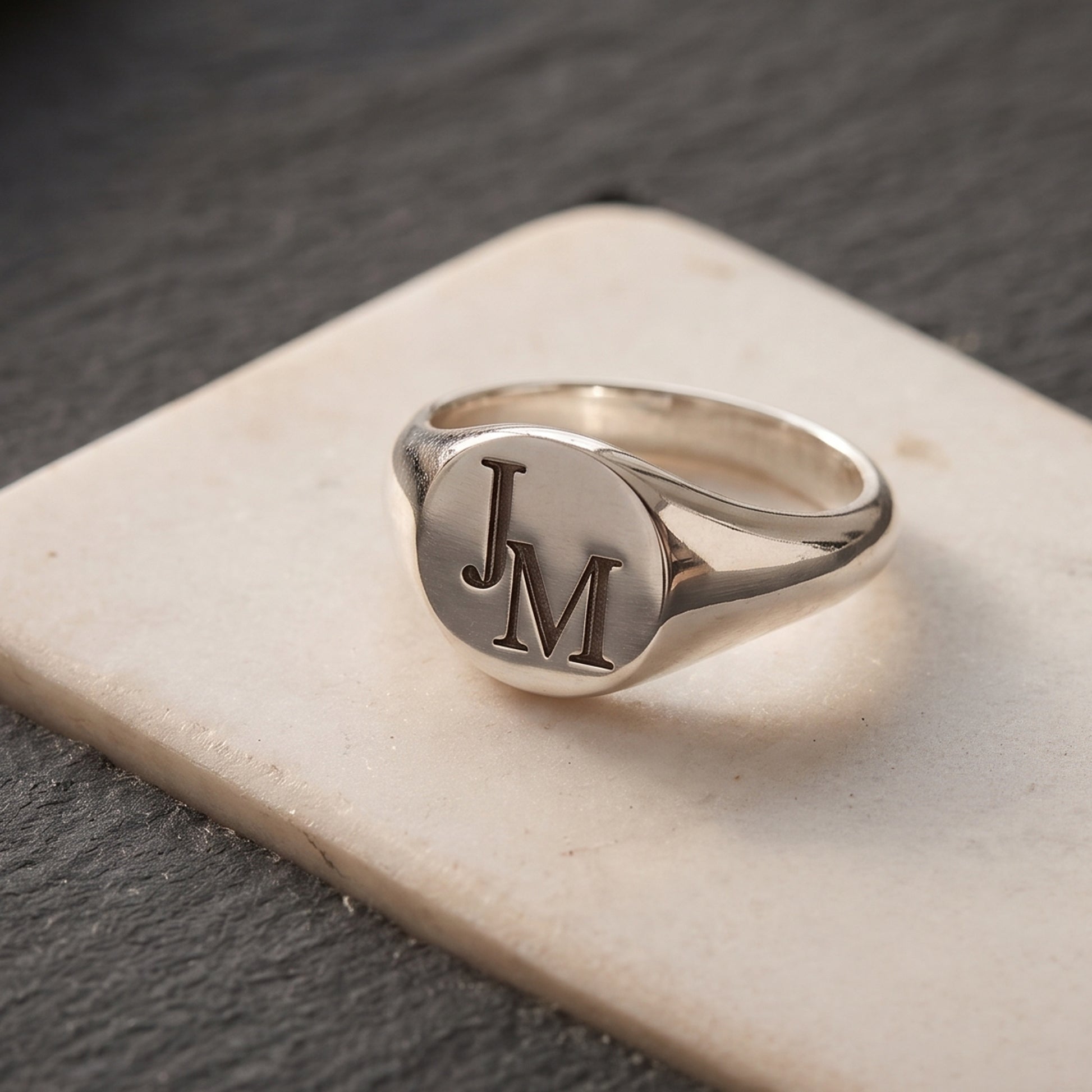 Silver ring with 'JM' initials on a stone surface