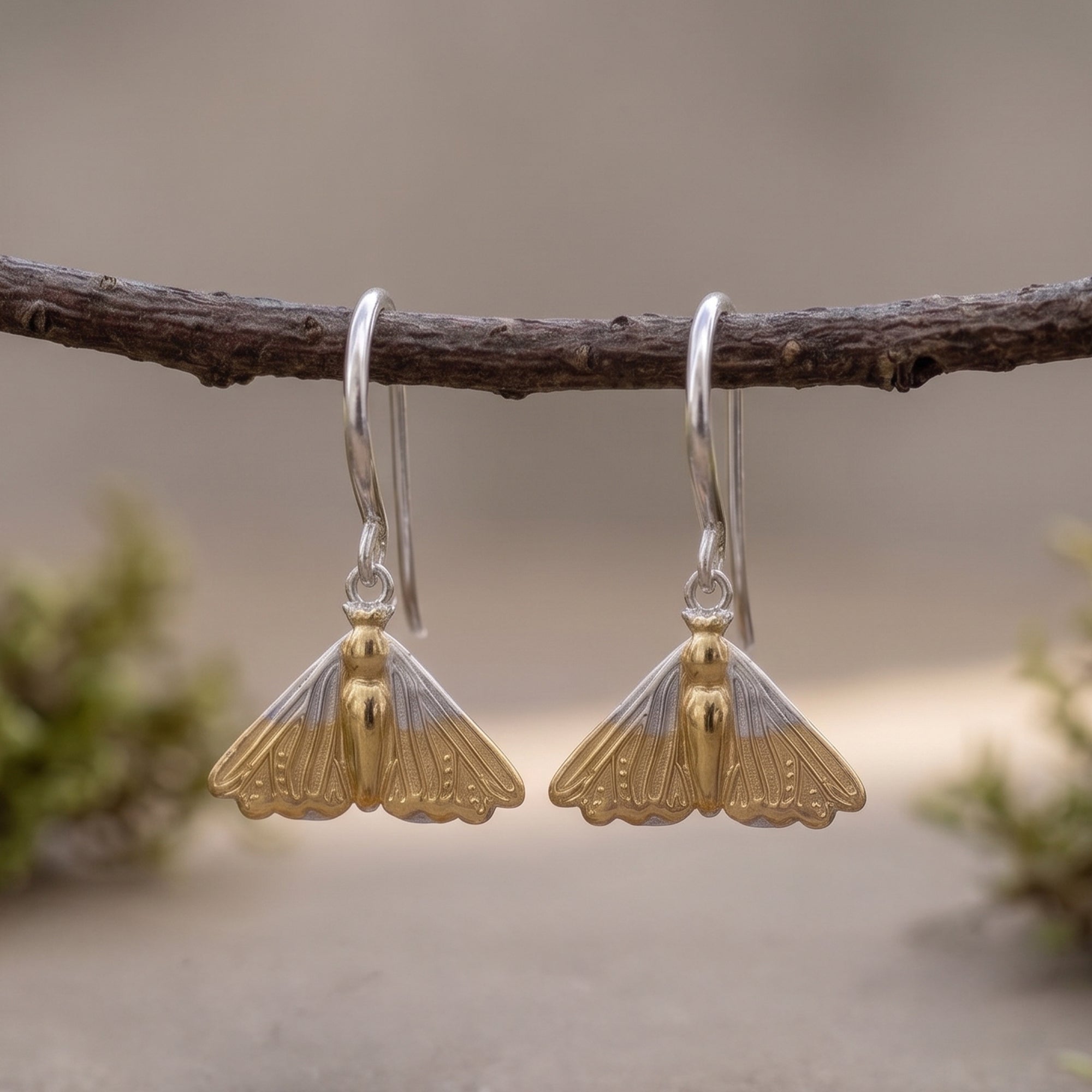 Gold and silver earrings hanging on a branch with a natural background