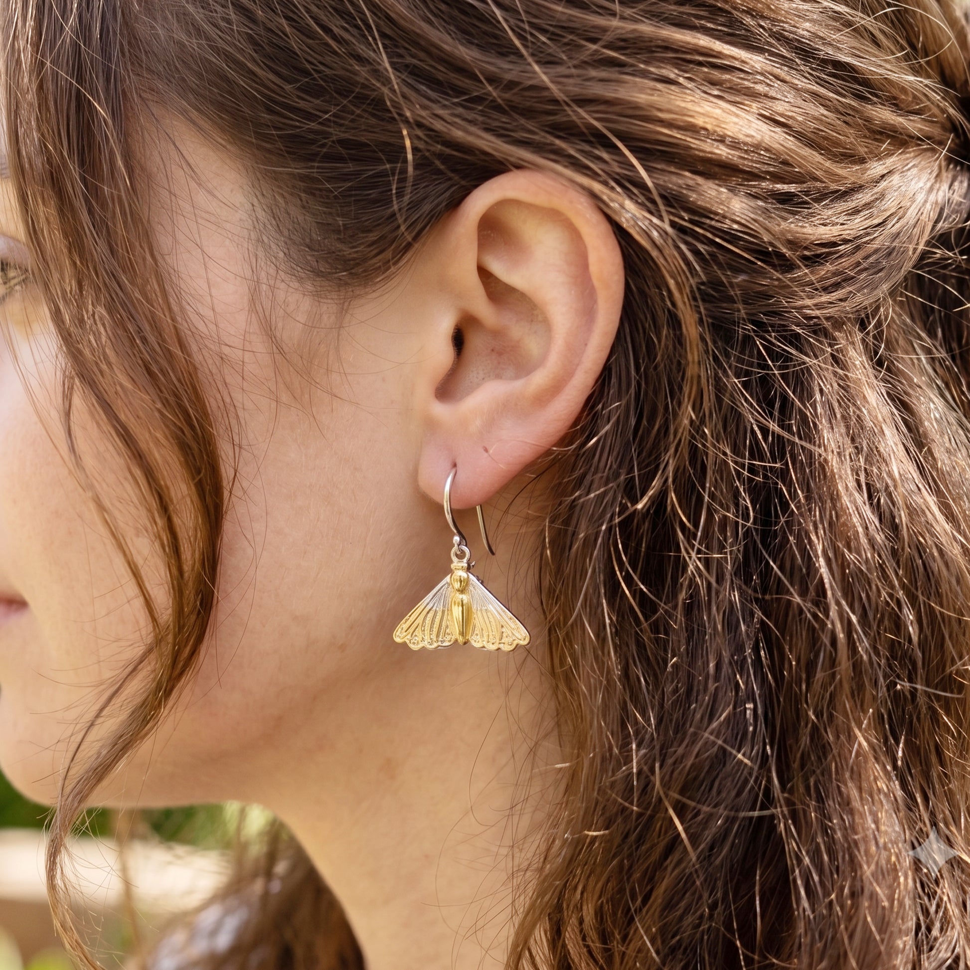 Close-up of a person wearing gold earrings with a blurred background