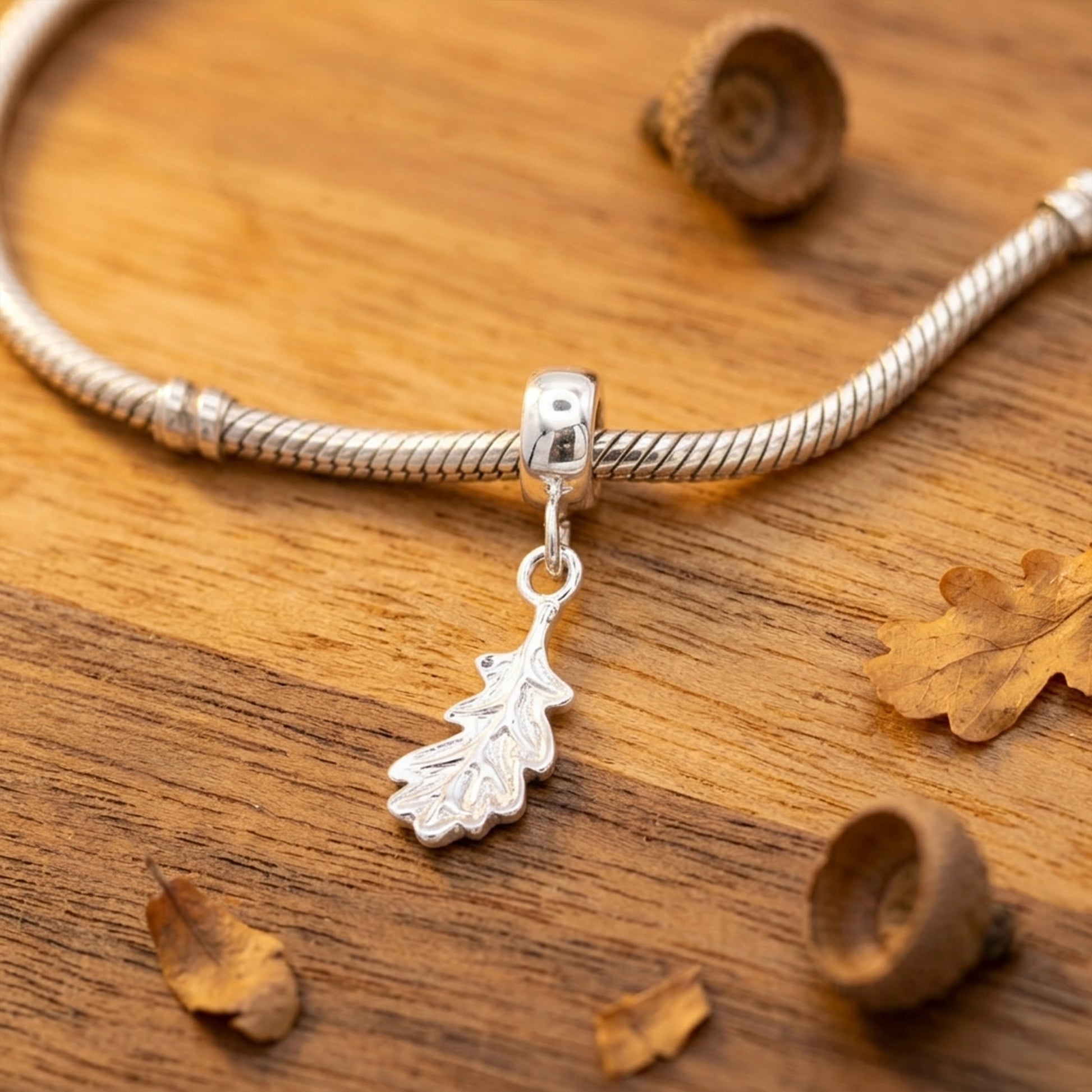Silver bracelet with a leaf charm on a wooden surface with acorns and leaves.