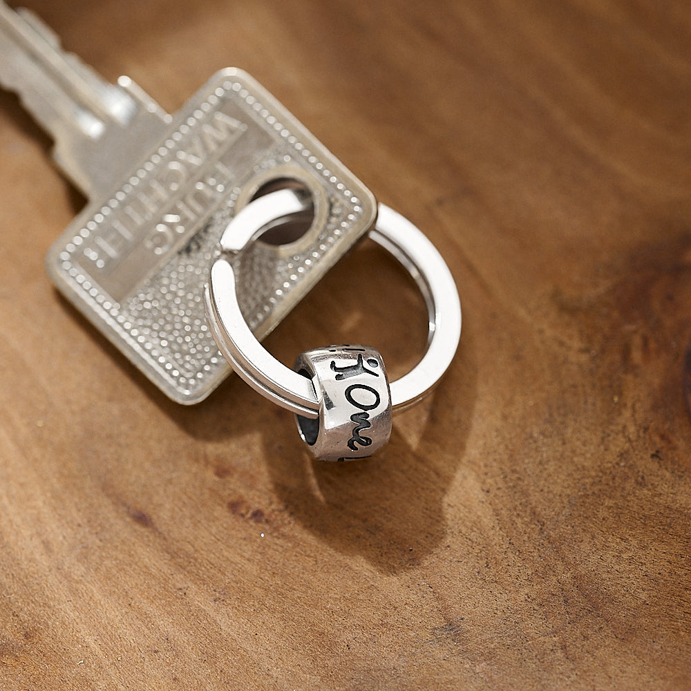 Silver keychain with a 'one life live it' charm on a wooden surface