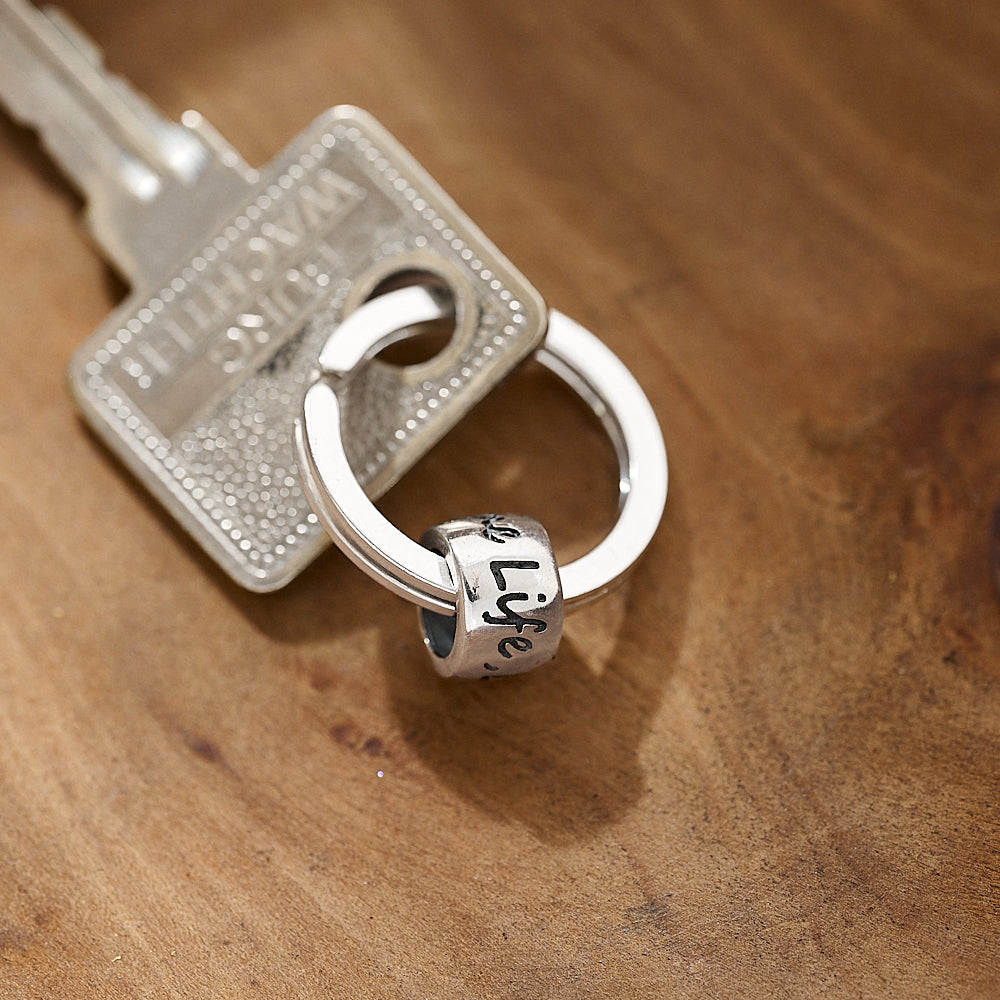 Silver key ring with a 'one life live it' charm on a wooden surface