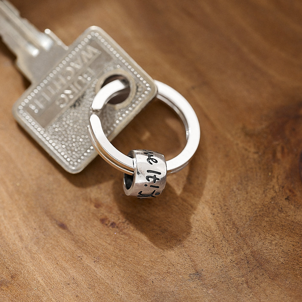 Silver keychain with a 'one life live it' charm on a wooden surface