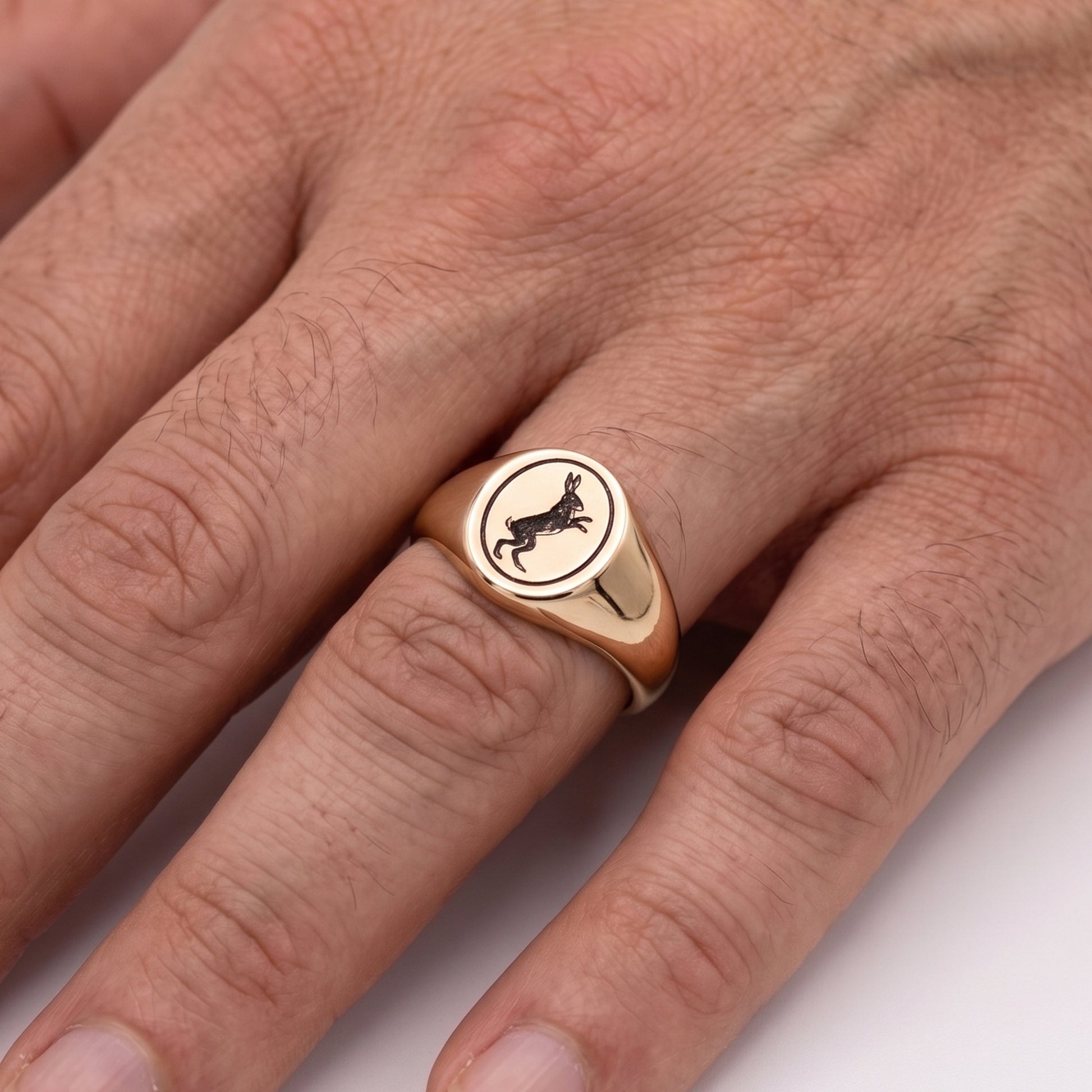 Rose gold ring with a hare rabbit emblem on a person's finger against a white background