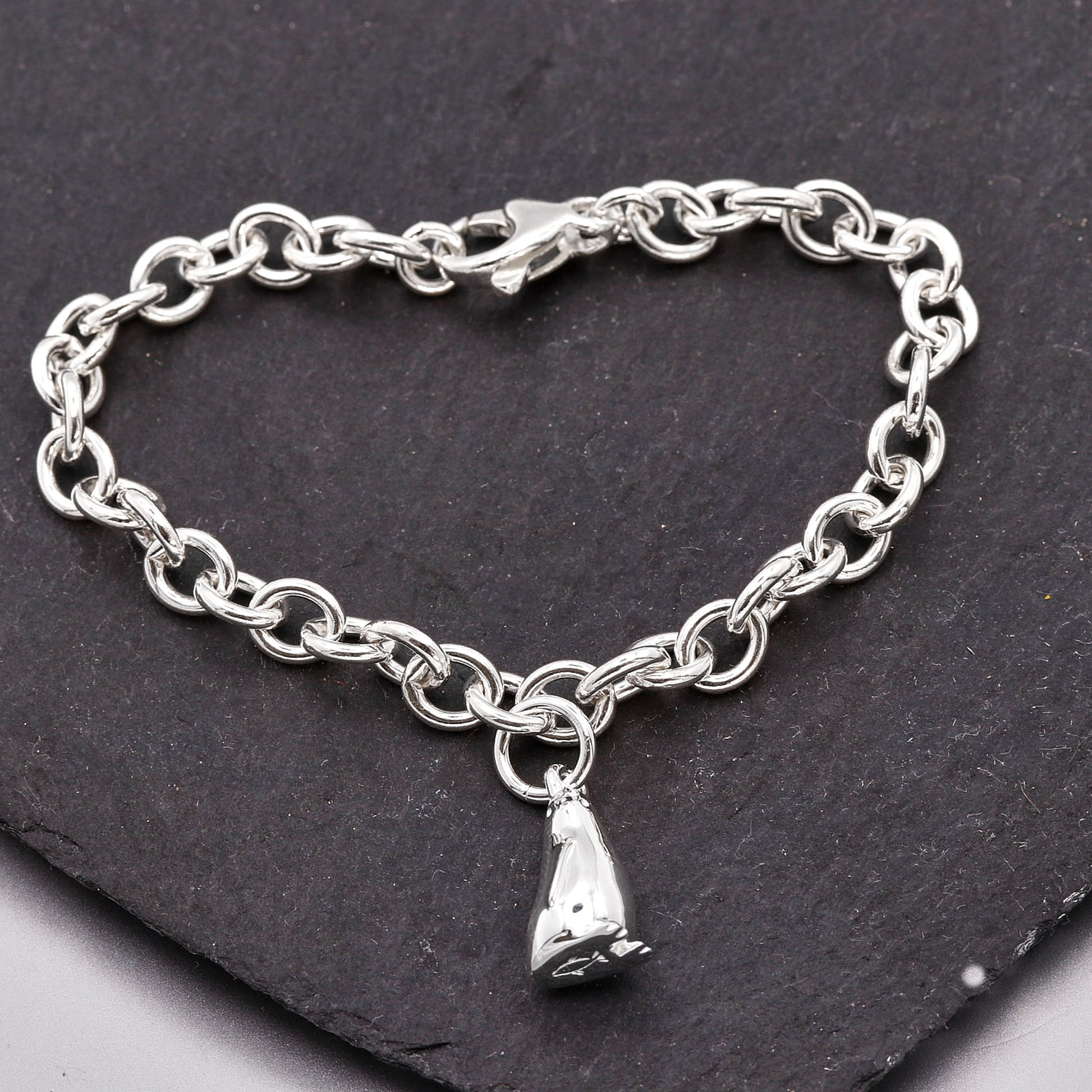 Silver chain bracelet with a penguin charm on a dark stone surface