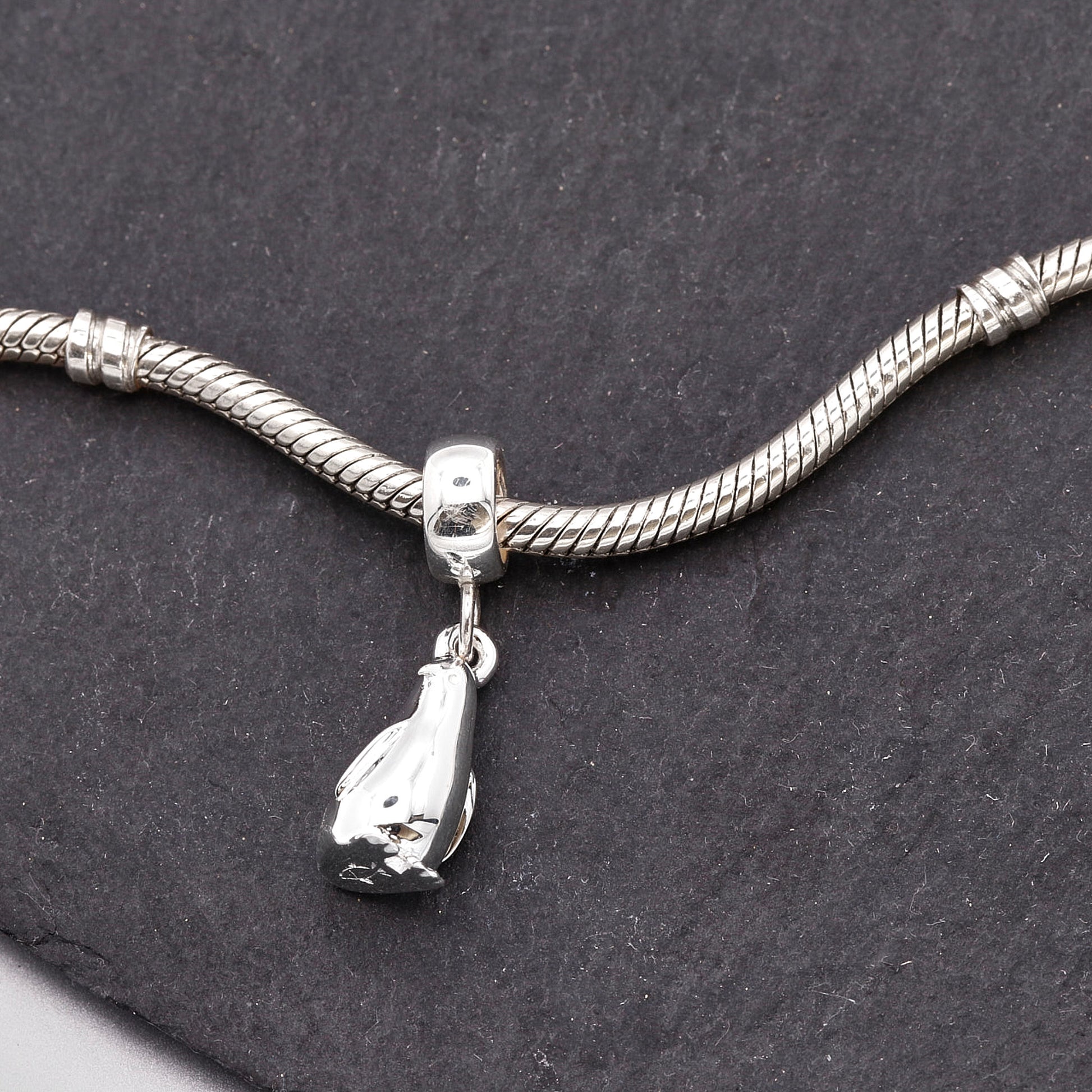 Silver snake chain bracelet with a penguin charm on a dark stone surface