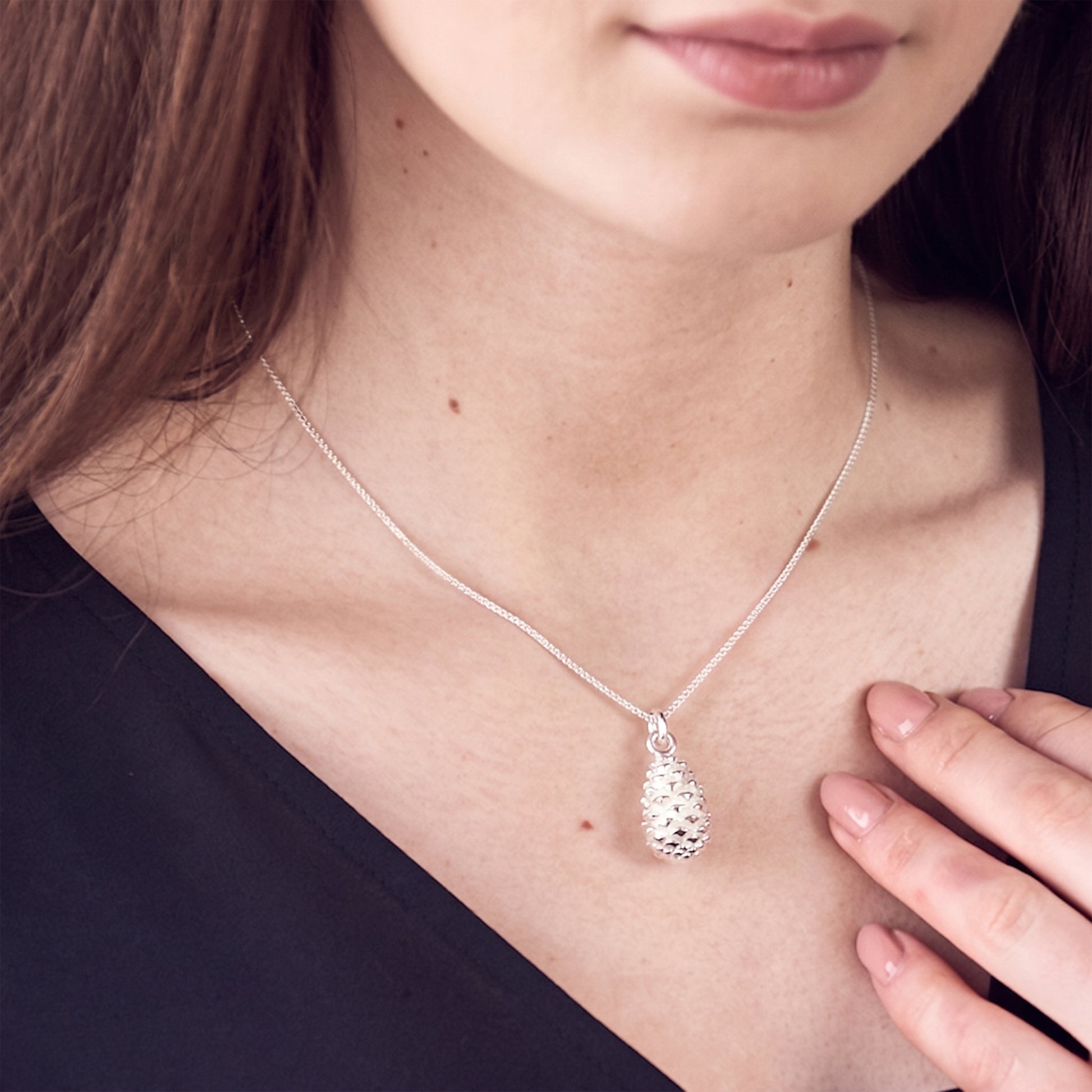 Silver necklace with a textured pine cone pendant worn by a person