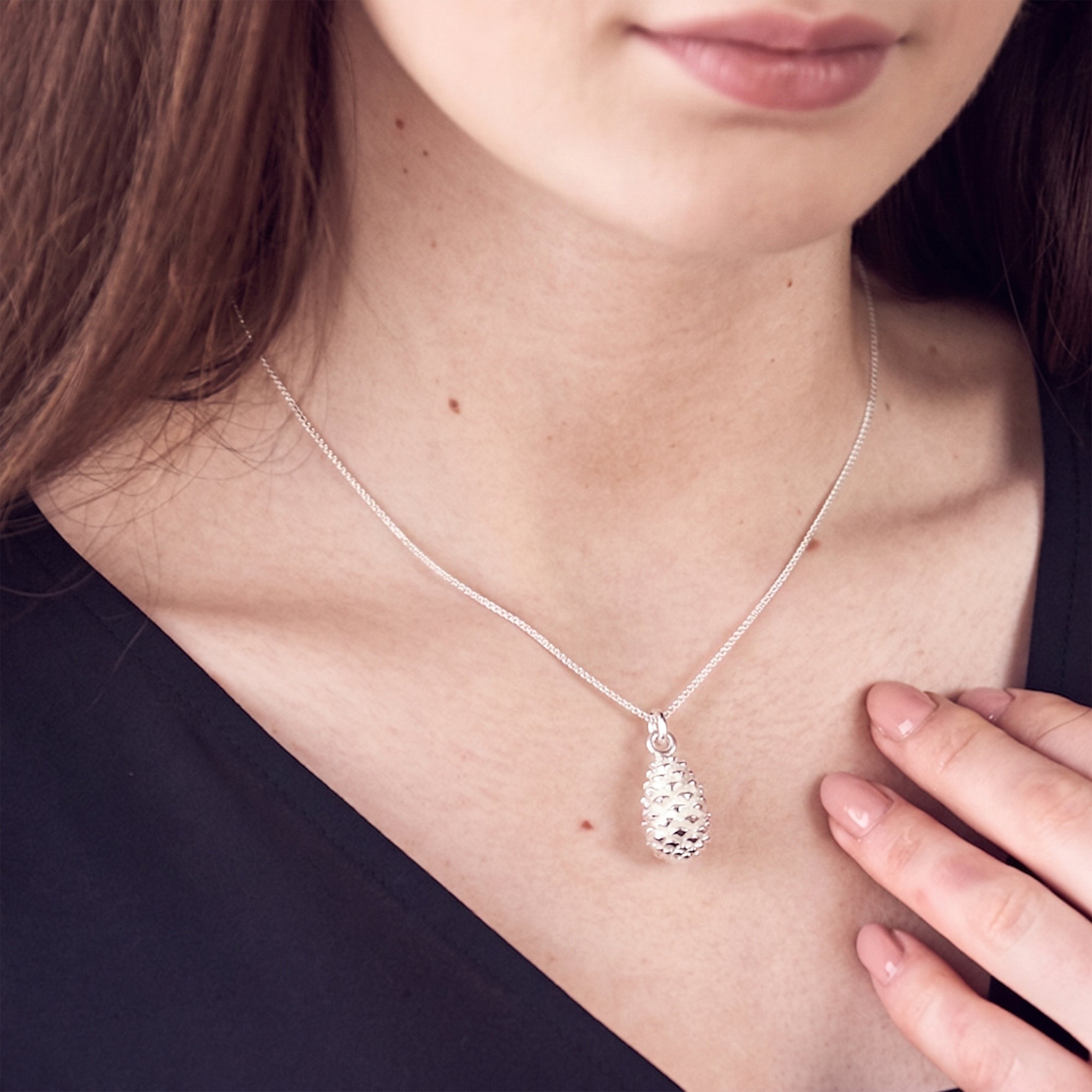 Silver necklace with a textured pine cone pendant worn by a person