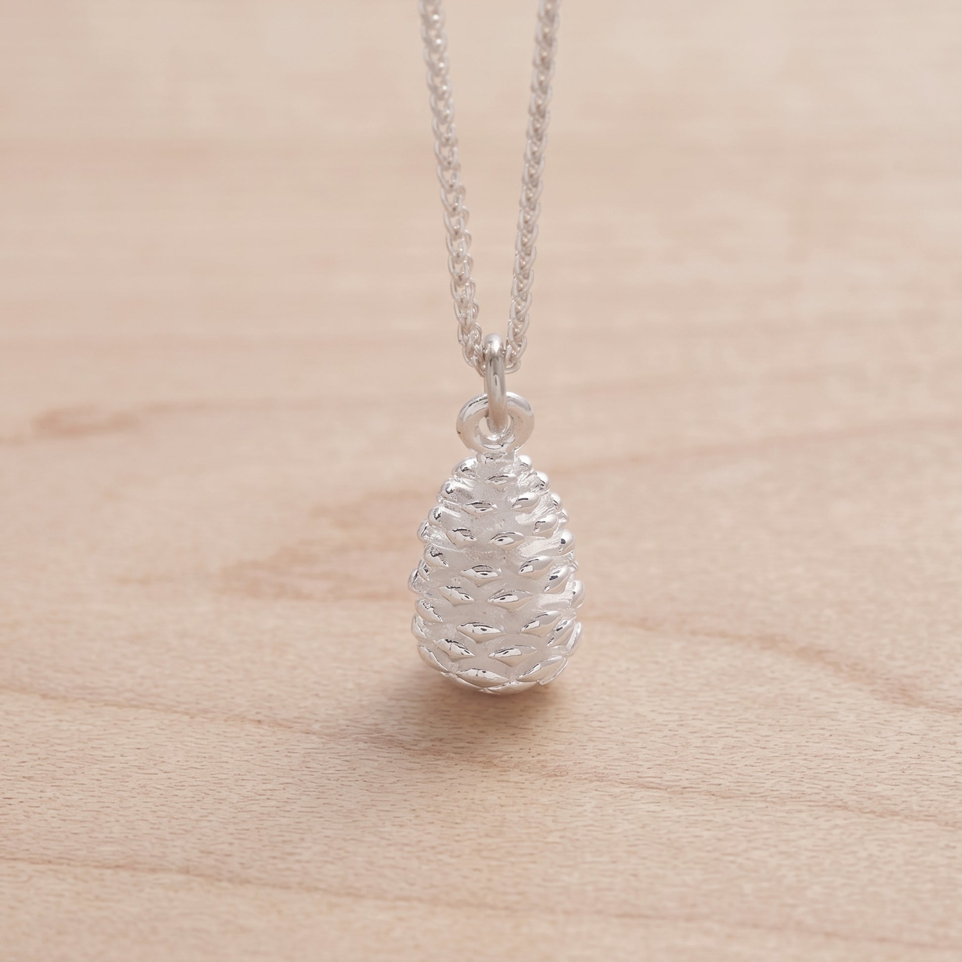 Silver pinecone pendant necklace on a light wood surface