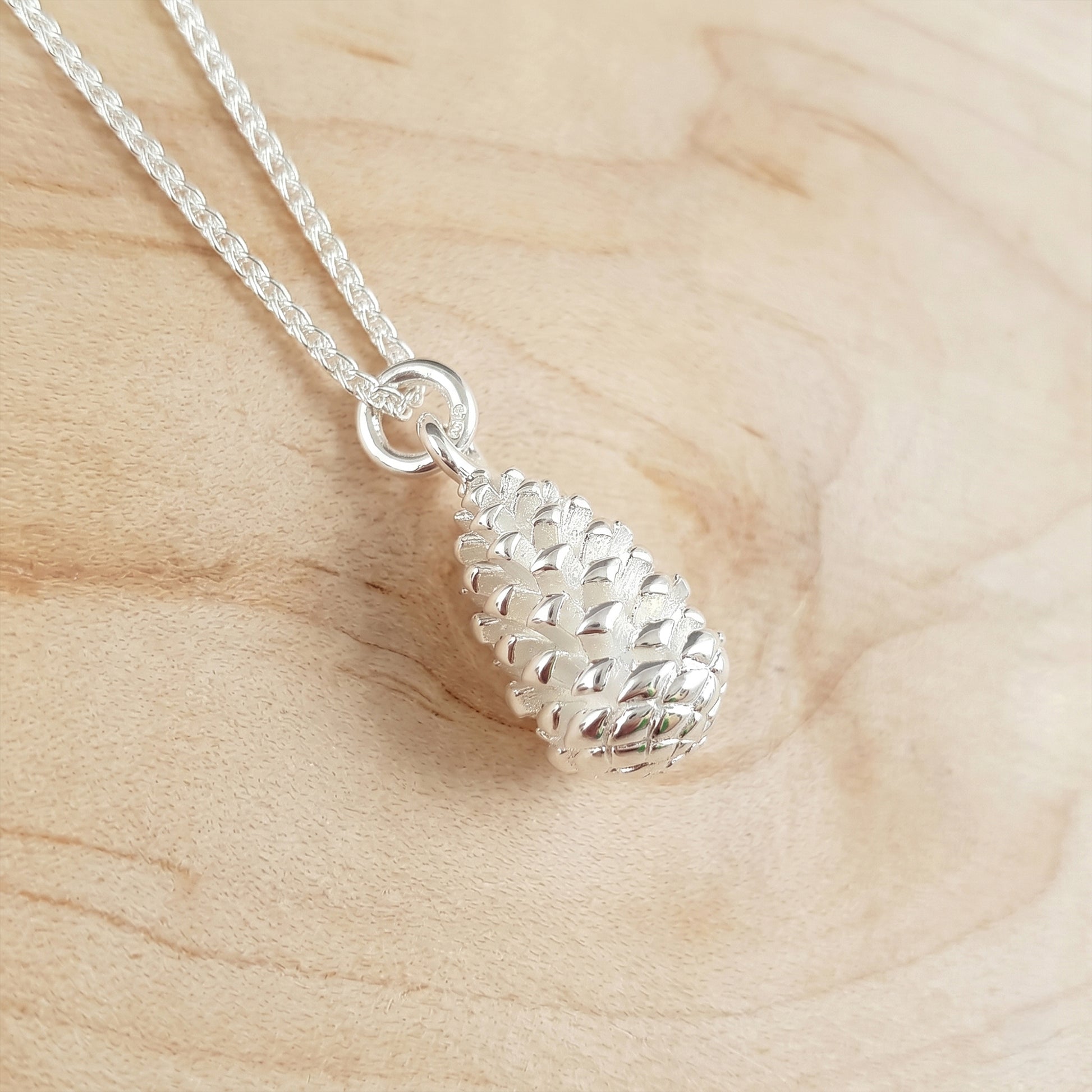 Silver pinecone pendant necklace on a wooden surface