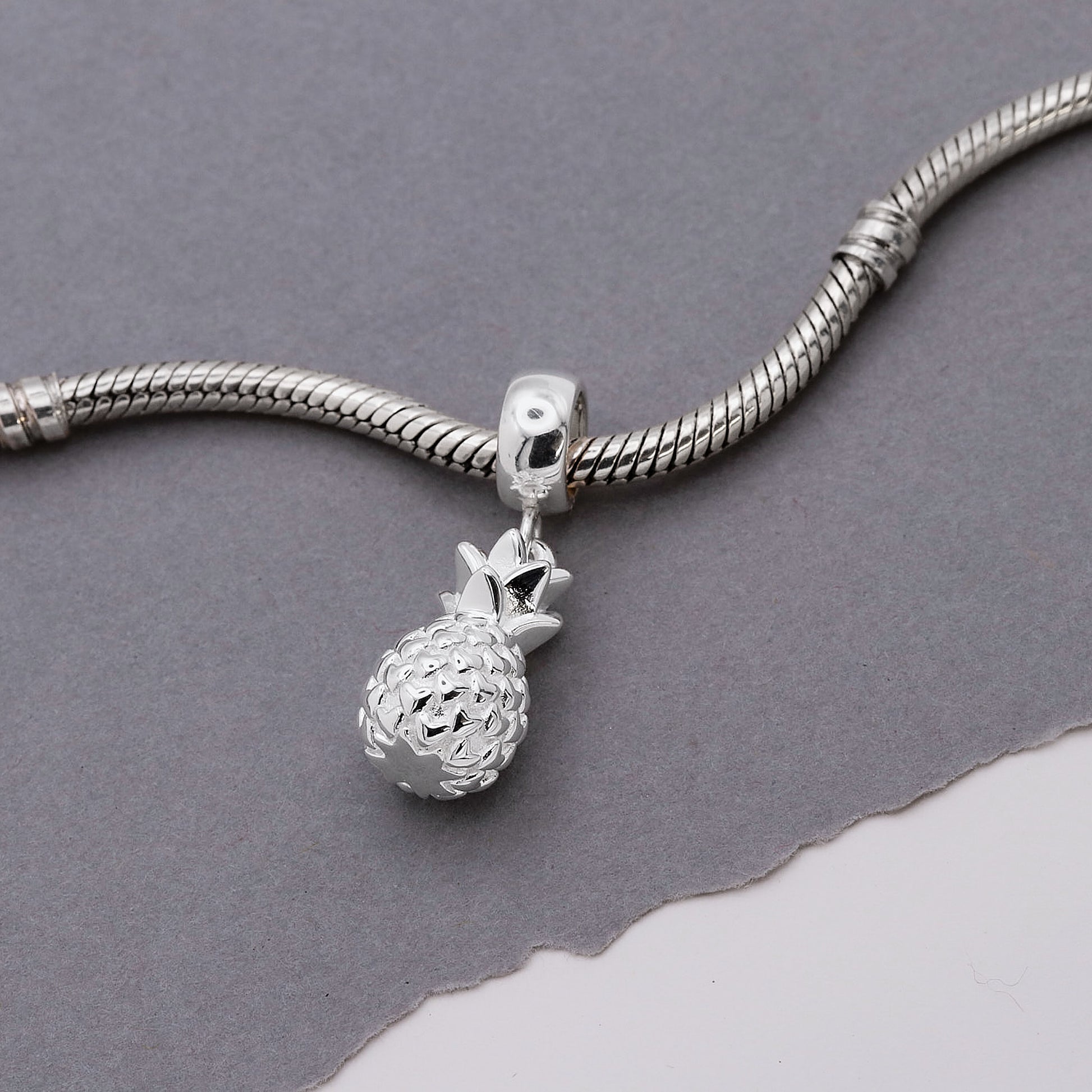 Silver pineapple charm on a snake chain against a gray background