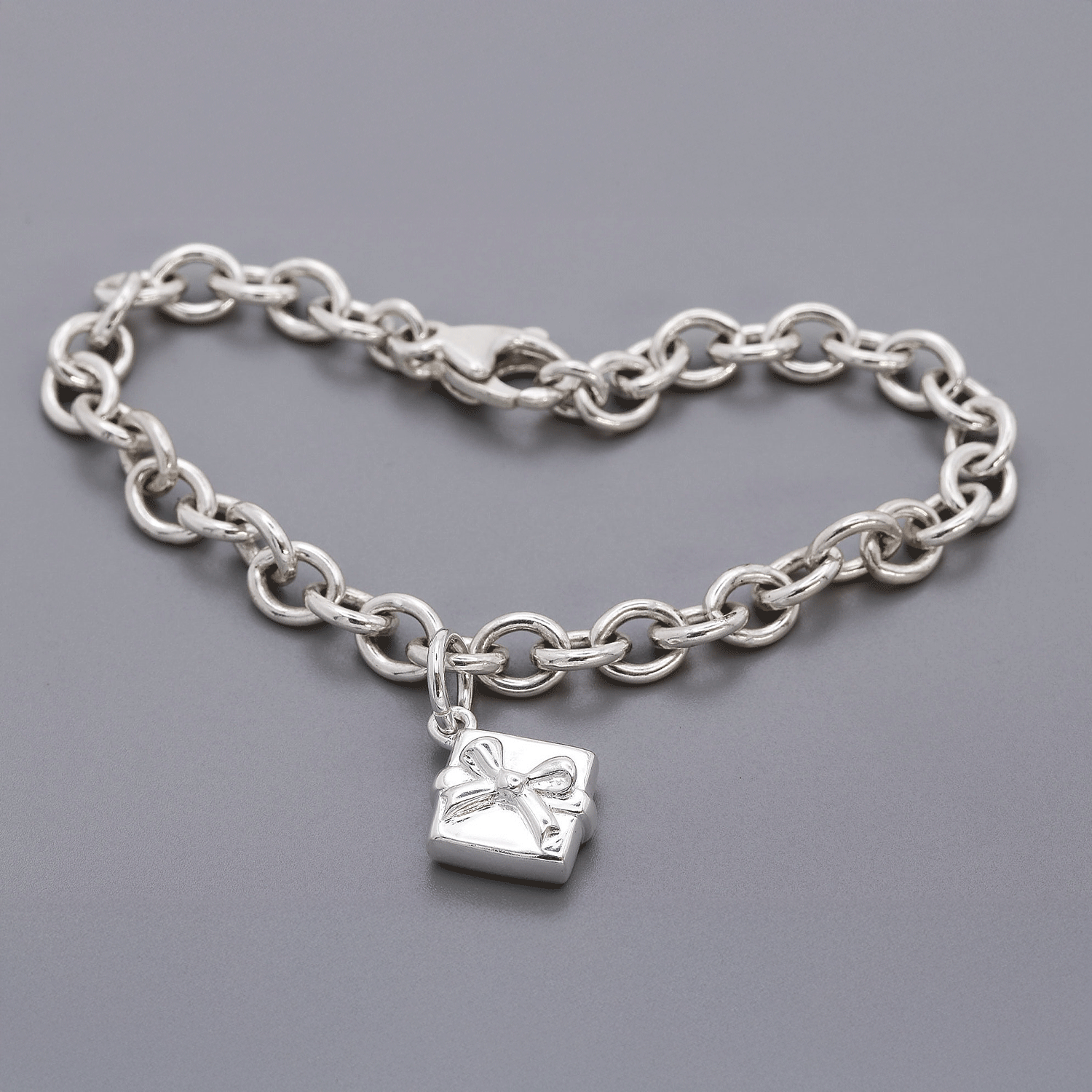 Silver chain bracelet with a present-shaped charm on a gray background