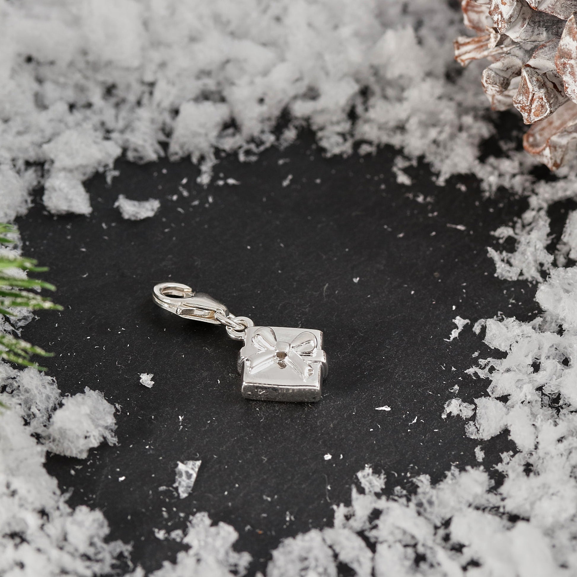 Silver charm resembling a wrapped gift on a dark surface with snow-like texture