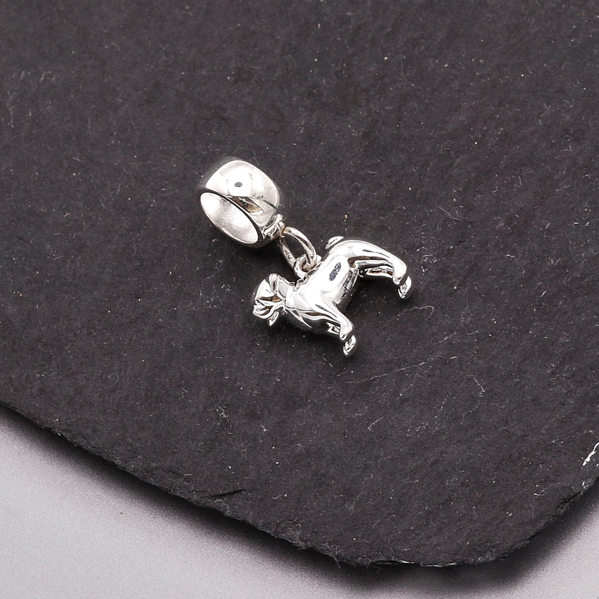 Silver pug dog charm on a black stone surface