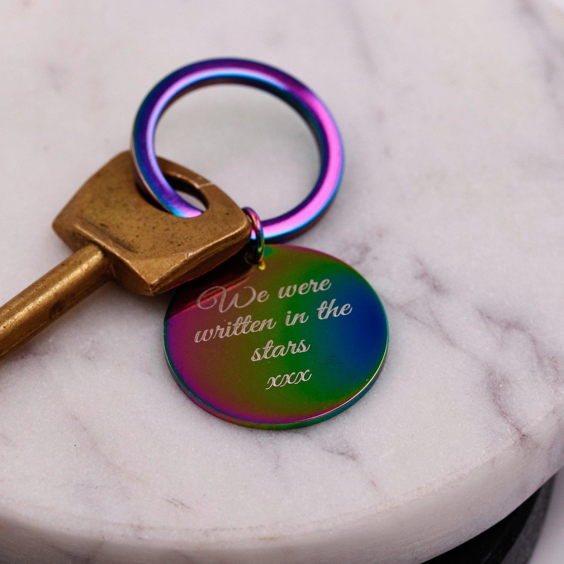 Keychain with a round tag that says 'We were written in the stars' on a marble surface.