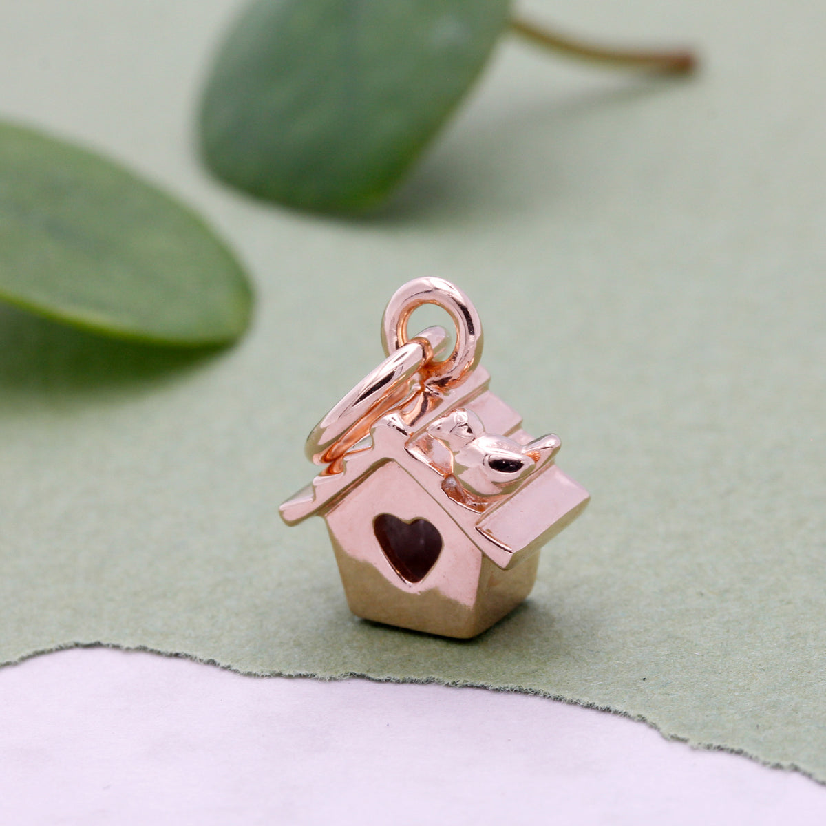 Rose gold-plated bird house charm with tiny bird perched on roof and heart entrance