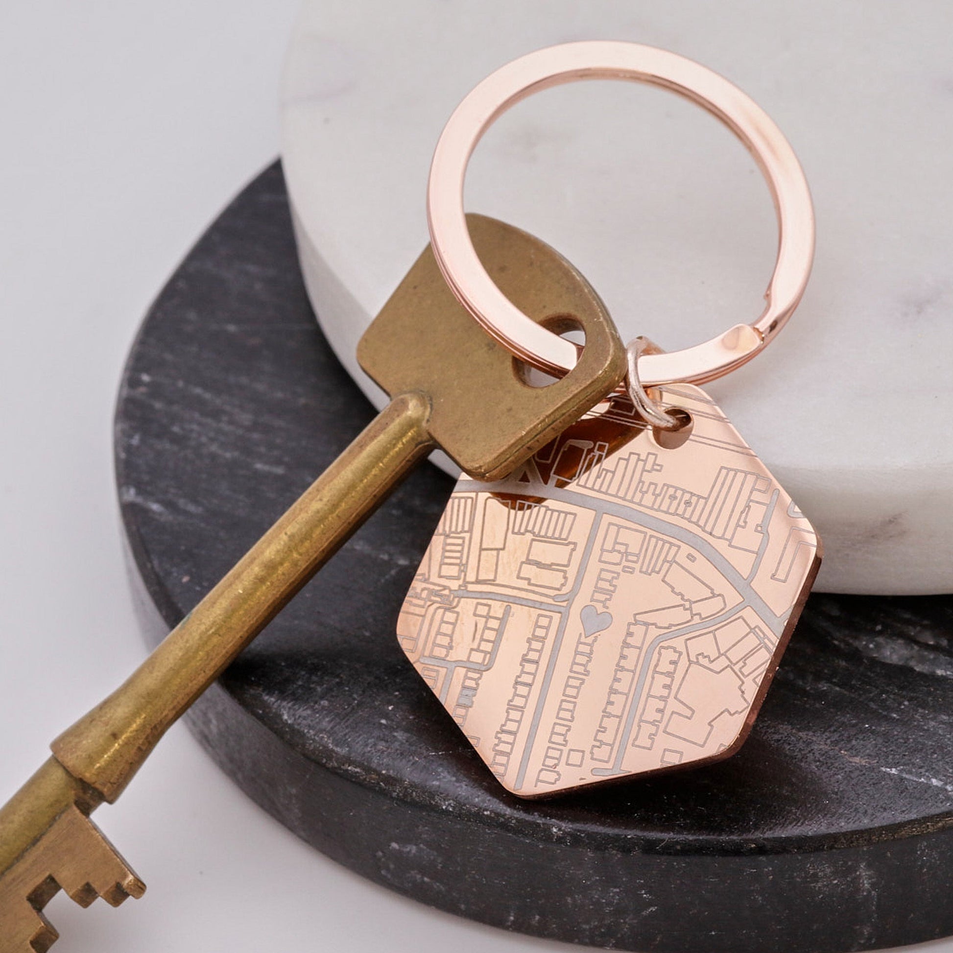 Rose gold keychain with a street map design on a black stand with a white background
