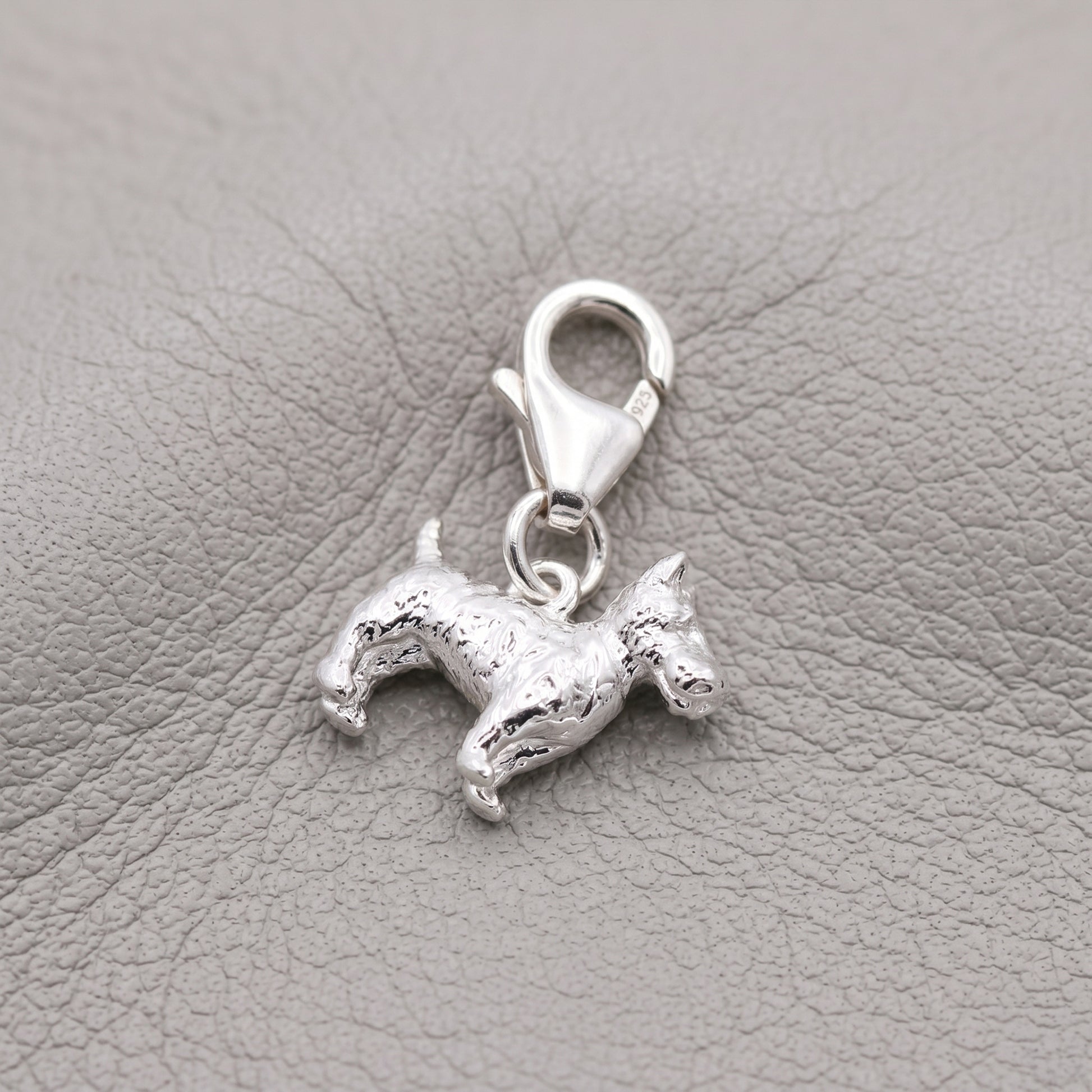 Silver scotty dog charm on a gray leather background