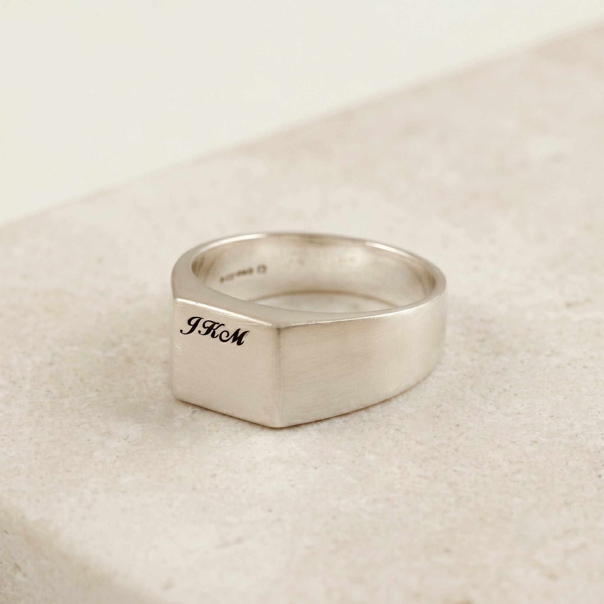 Silver ring with engraved initials on a beige fabric background