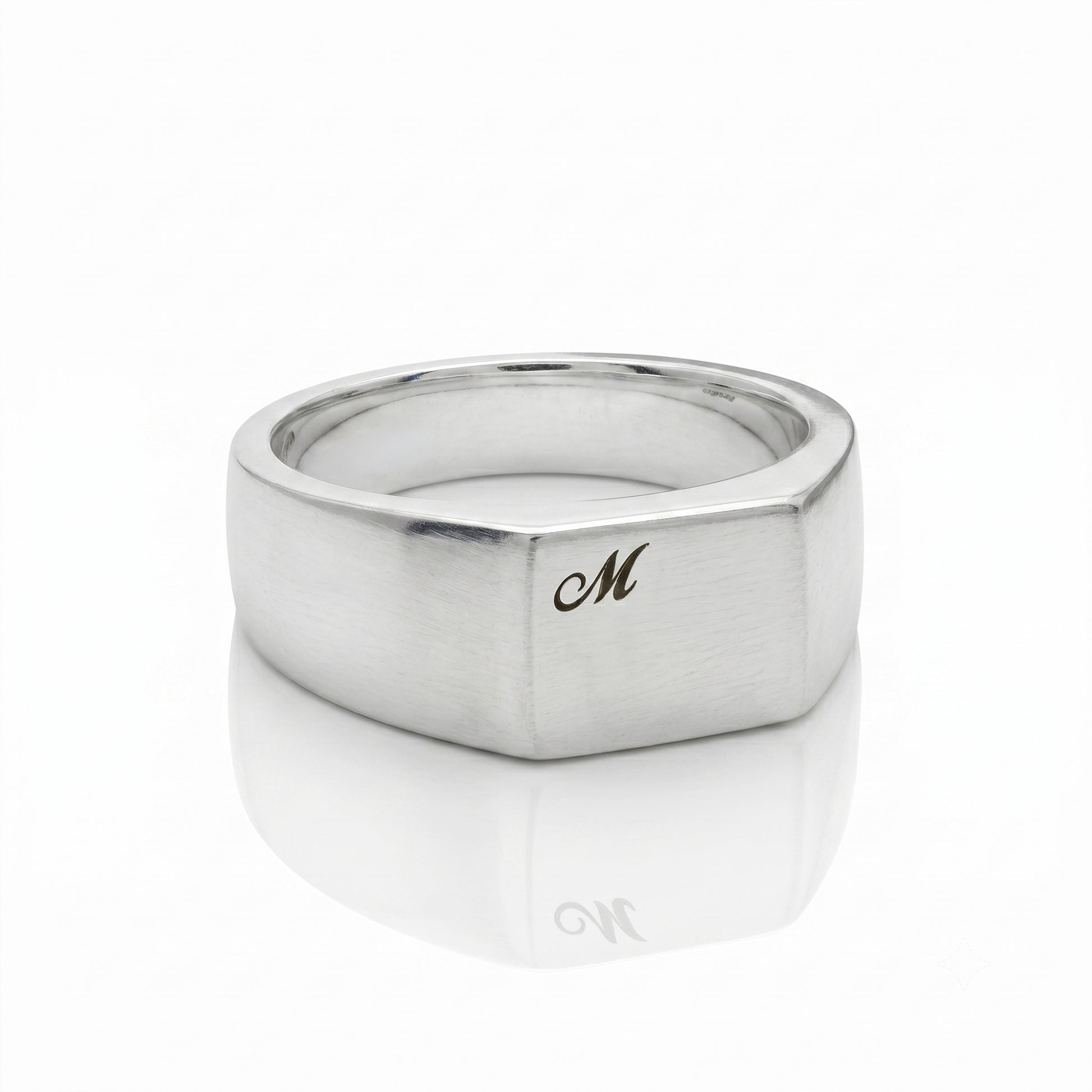 Silver ring with a gold 'M' on a white background
