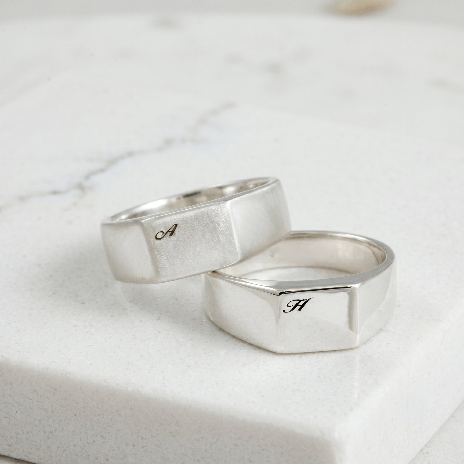 Two silver rings with engraved letters on a light marble background