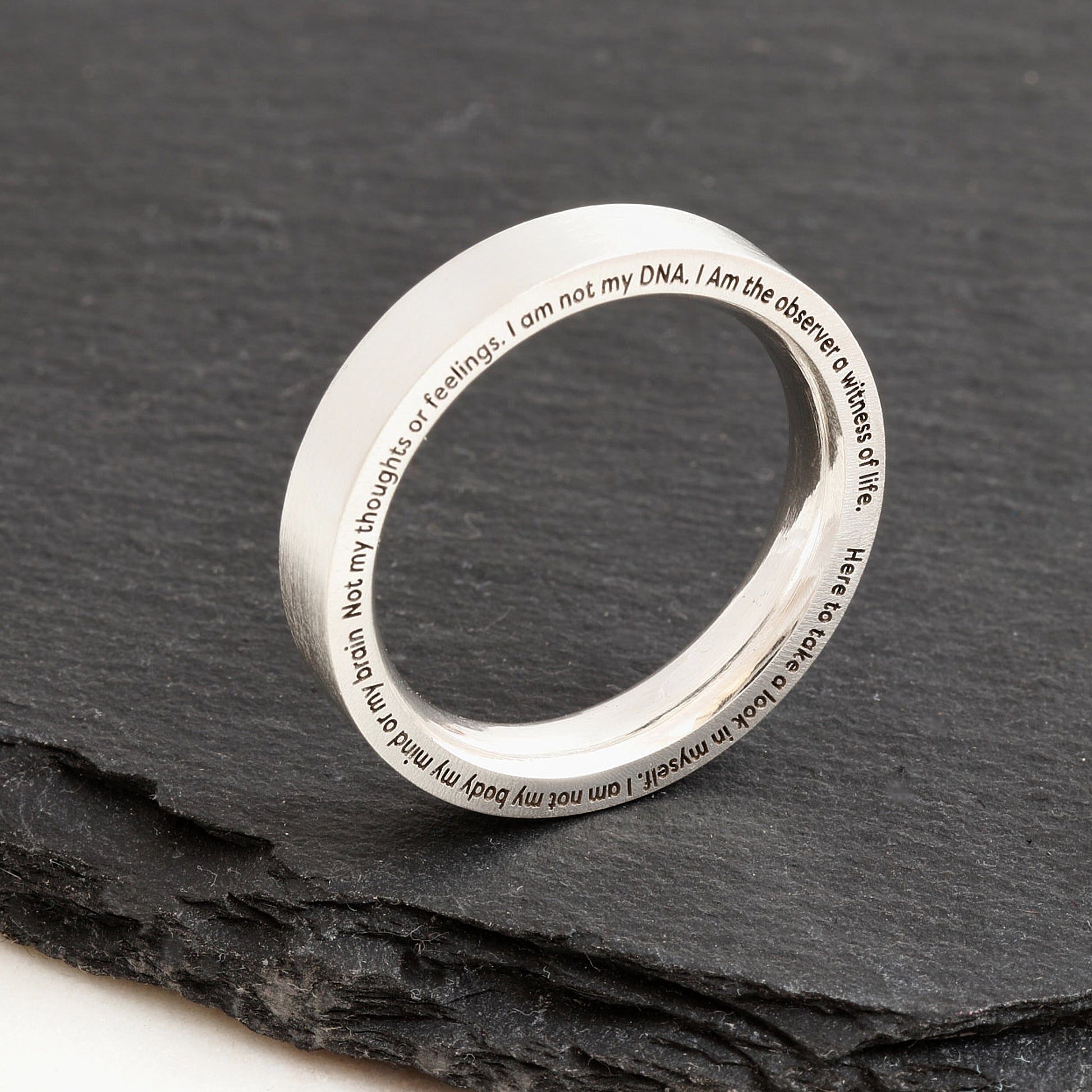 Silver ring with engraved text on a dark stone surface