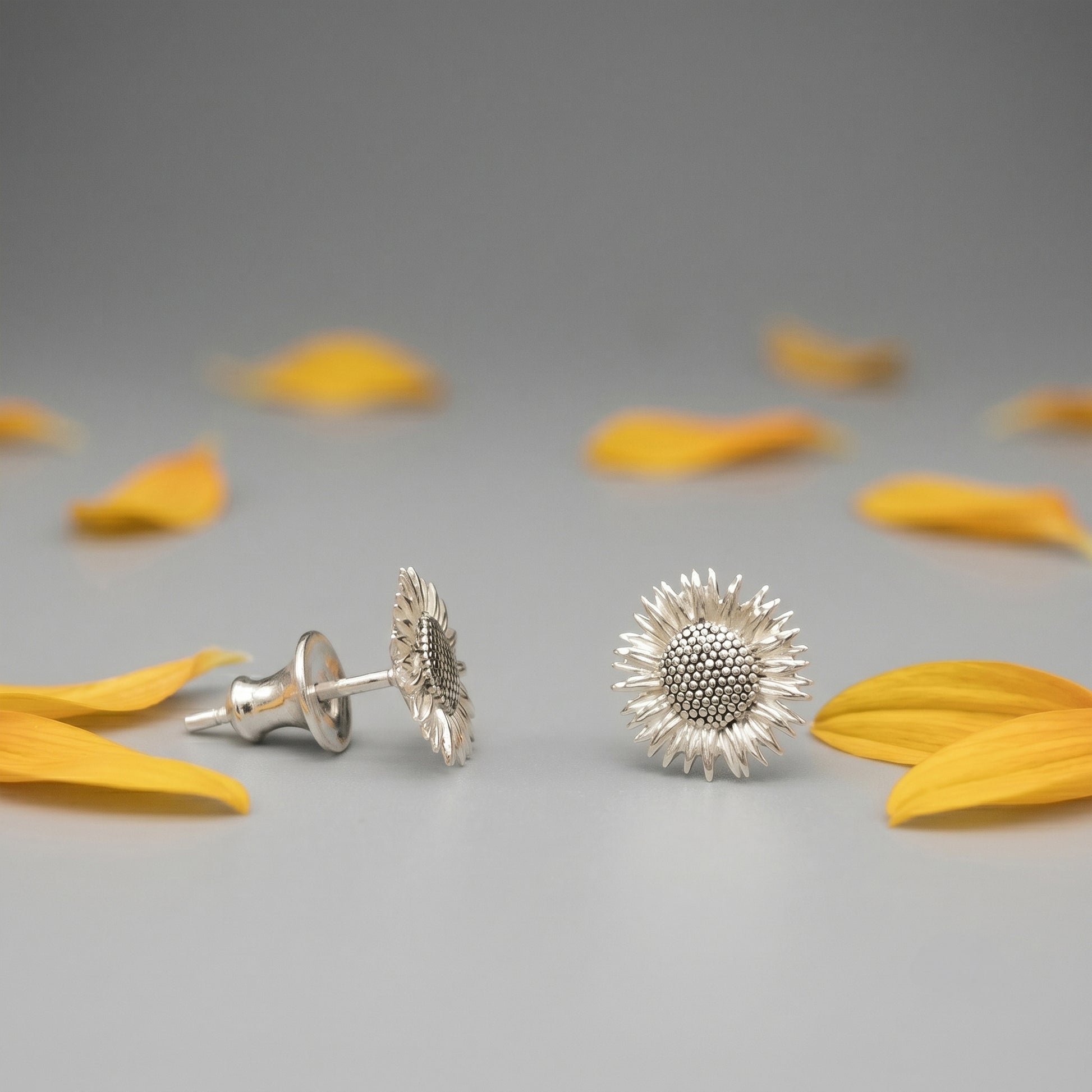 Silver sunflower-shaped earrings on a gray background with yellow petals.