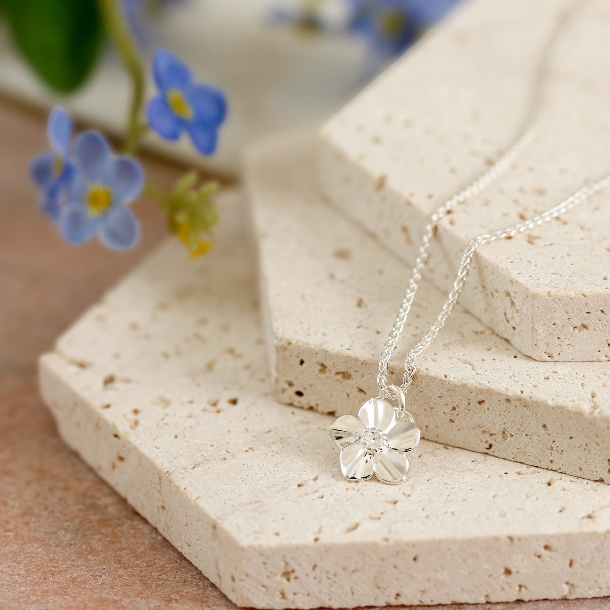 Silver necklace with a flower pendant on a textured surface with flowers in the background