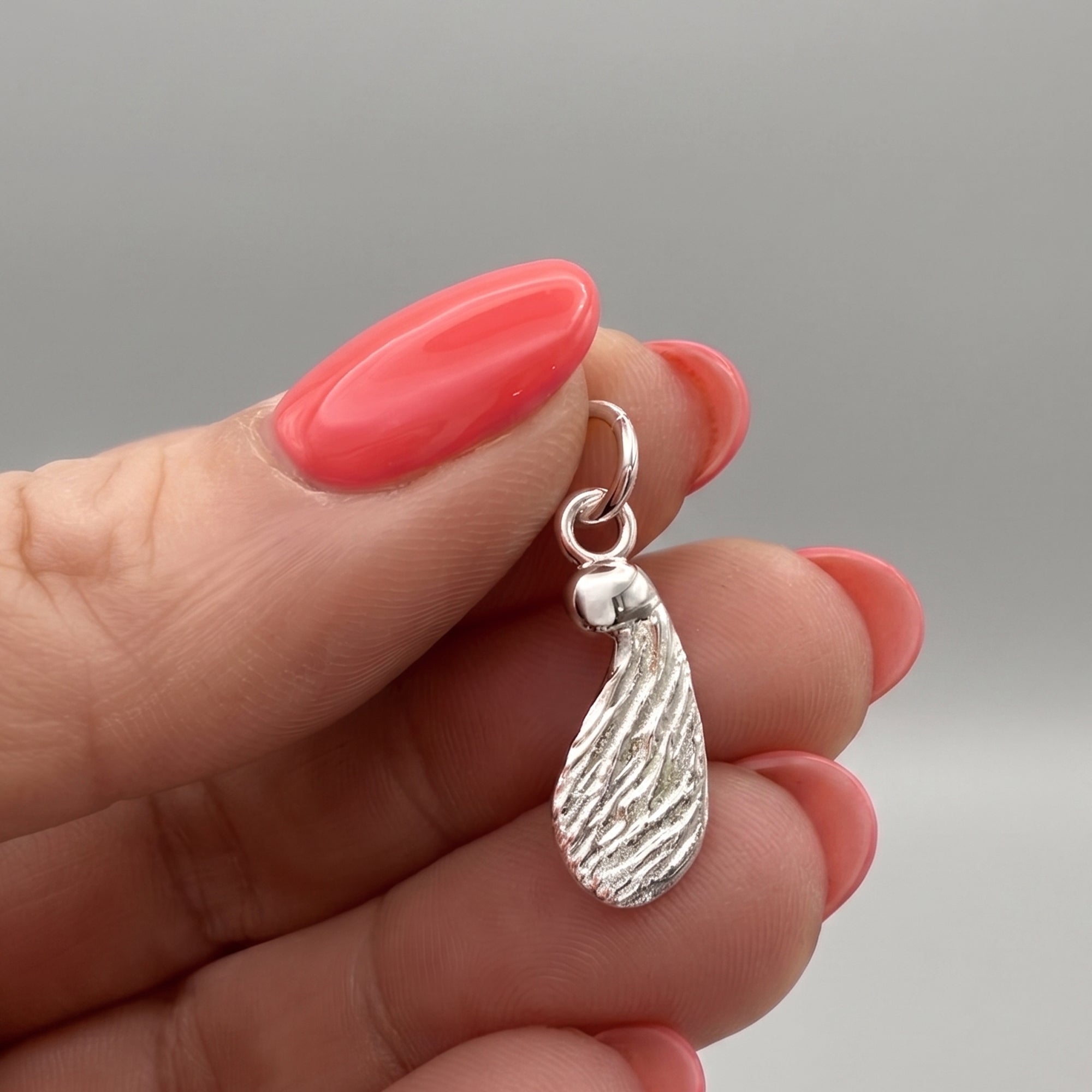 Silver seed-shaped pendant charm in a womans hands