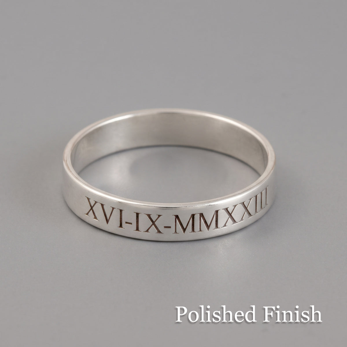 A polished silver band ring engraved with the Roman numerals 'XVI-IX-MMMXXIII' on a neutral gray background, with 'Polished Finish' text overlay in the bottom right corner.
